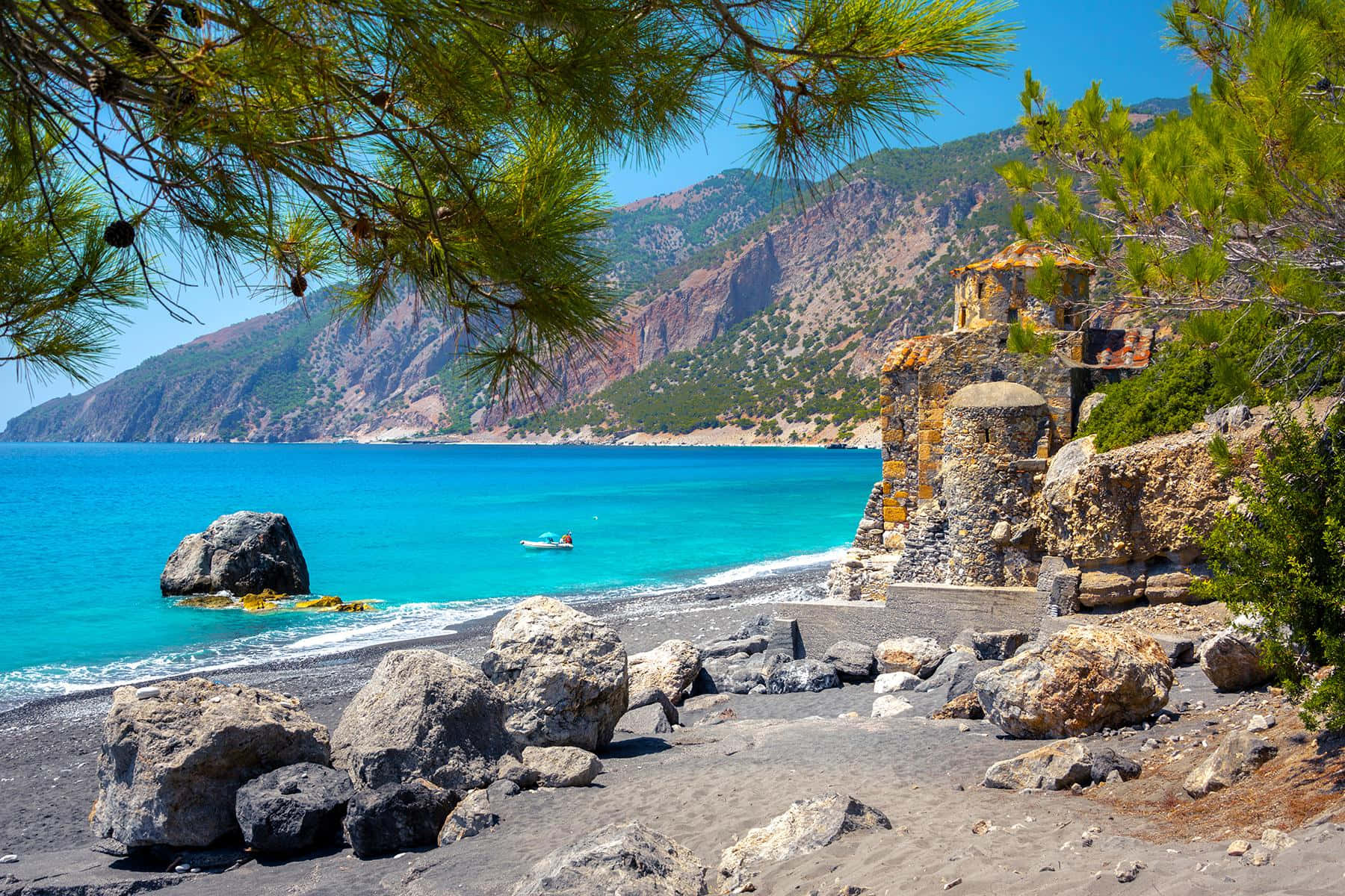 Greek Beach 桌布 壁紙 — 充滿活力的碧綠海水與松枝環繞的岩石海岸相遇，懸崖上有一座石砌小教堂，在清澈的藍天下。