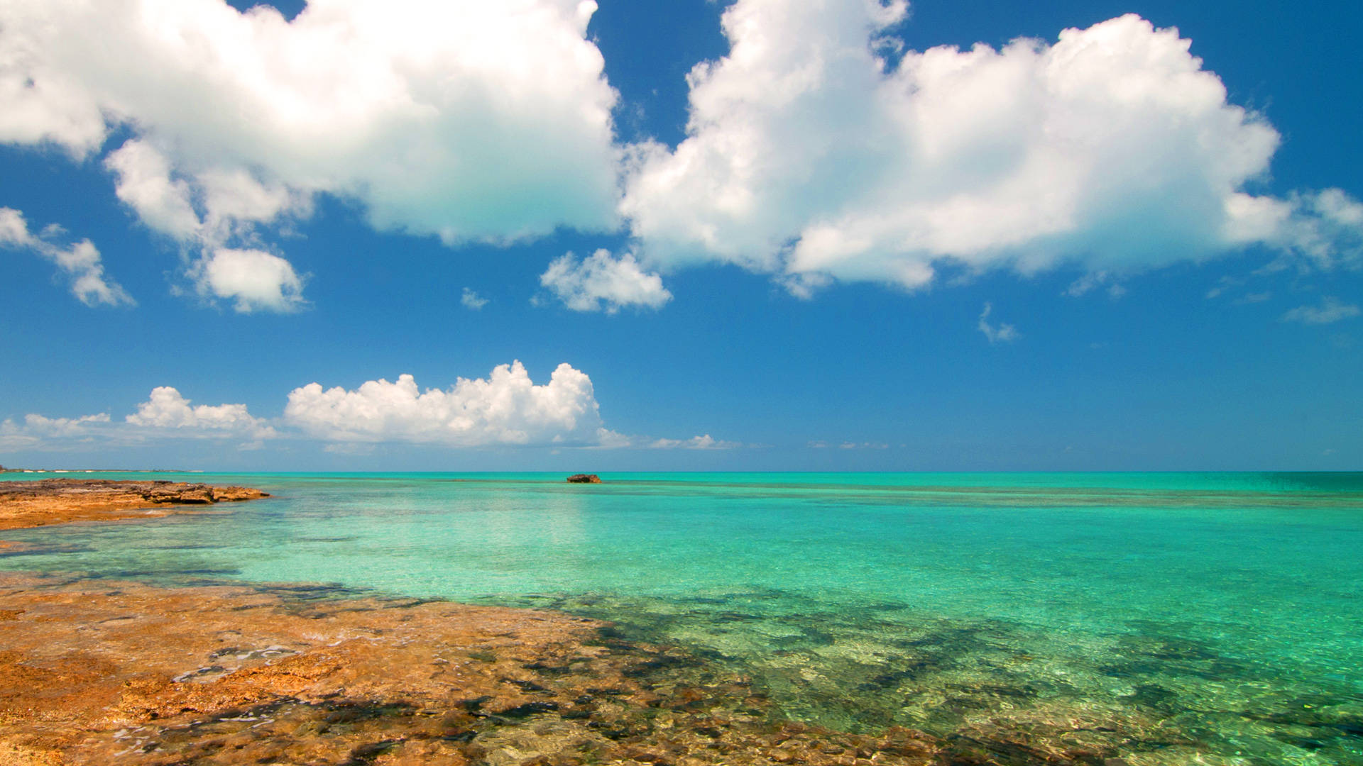 Nassau Bahamas 桌布 壁紙 — 充滿活力的碧綠海水輕輕拍打著陽光溫暖的珊瑚海岸，上方是點綴著蓬鬆白雲的燦爛藍天。