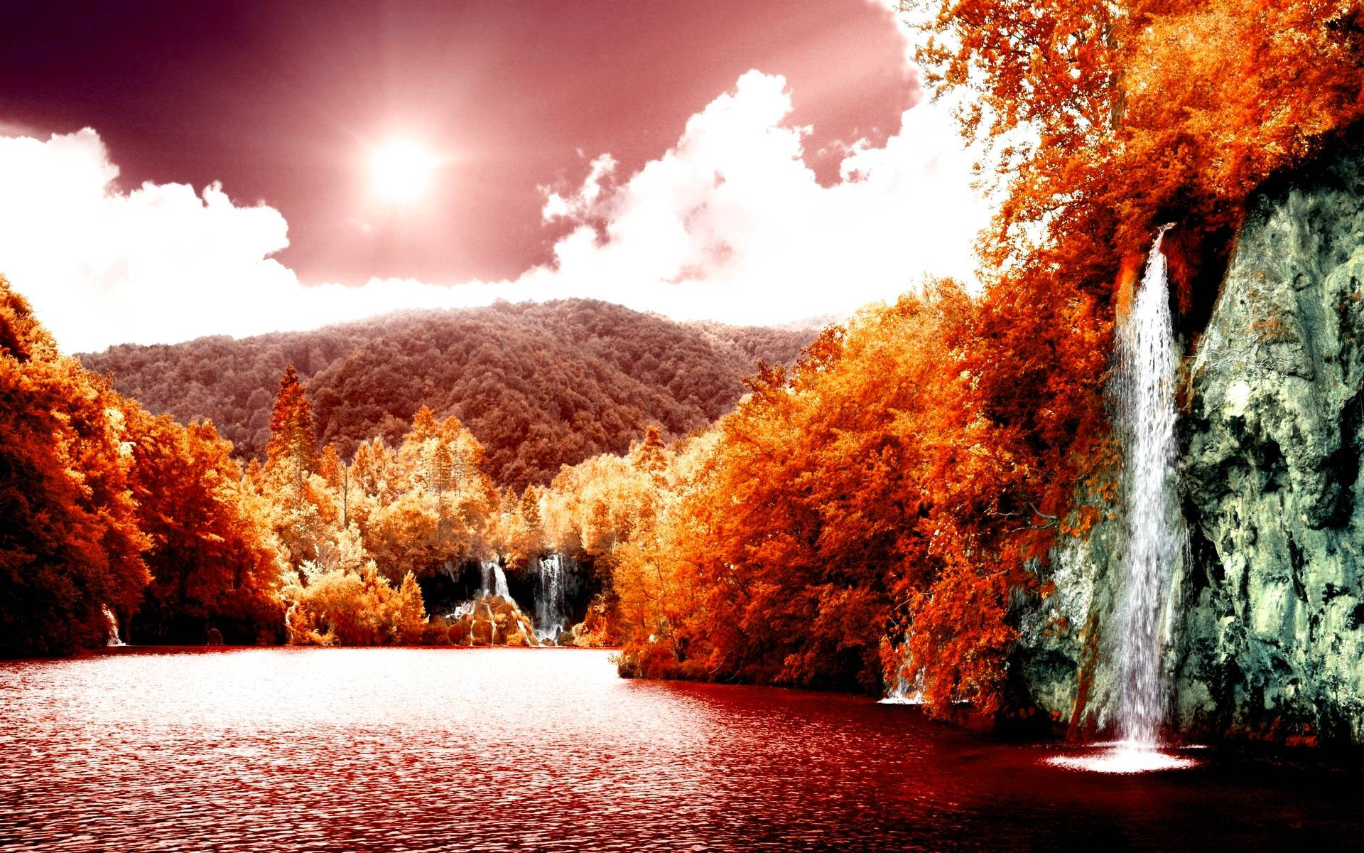 Autumn Season 桌布 壁紙 — 充滿活力的秋日森林與層疊瀑布，在戲劇性的陽光天空下倒映在平靜的湖面上。