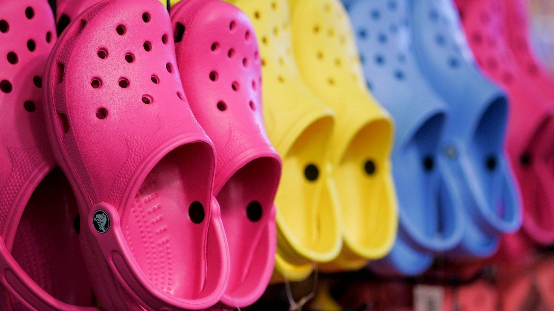 Crocs 桌布 壁紙 — 充滿活力的粉紅色、黃色和藍色Crocs鞋整齊排列在零售展示中，景深較淺。