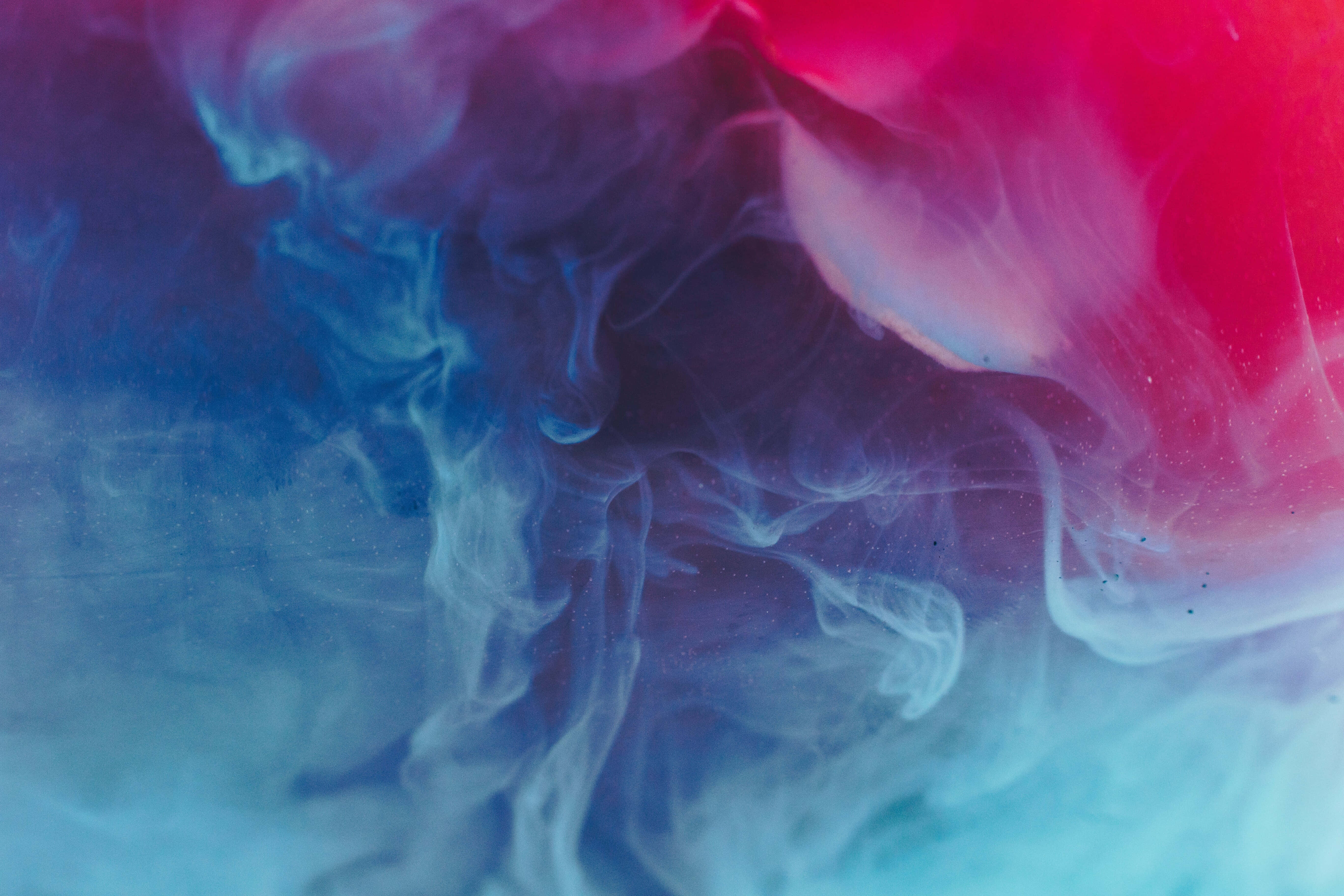Pink iPad Pro 桌布 壁紙 — 充滿活力的粉紅色和藍色墨水漩渦在深色背景上融合成空靈的煙霧。