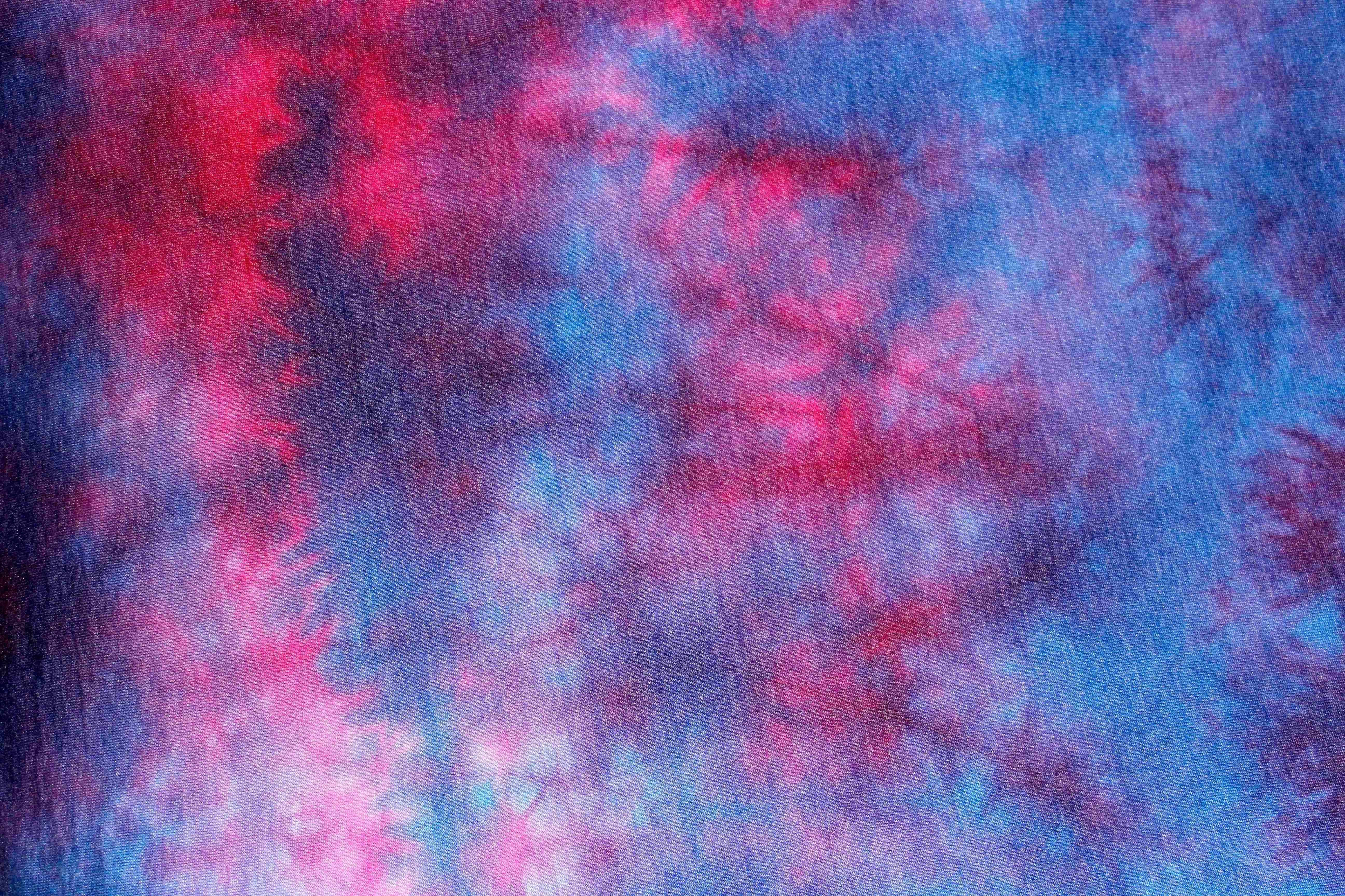 扎染 桌布 壁紙 — 充滿活力的粉紅色和藍色紮染布料，帶有漩渦圖案和紋理纖維。