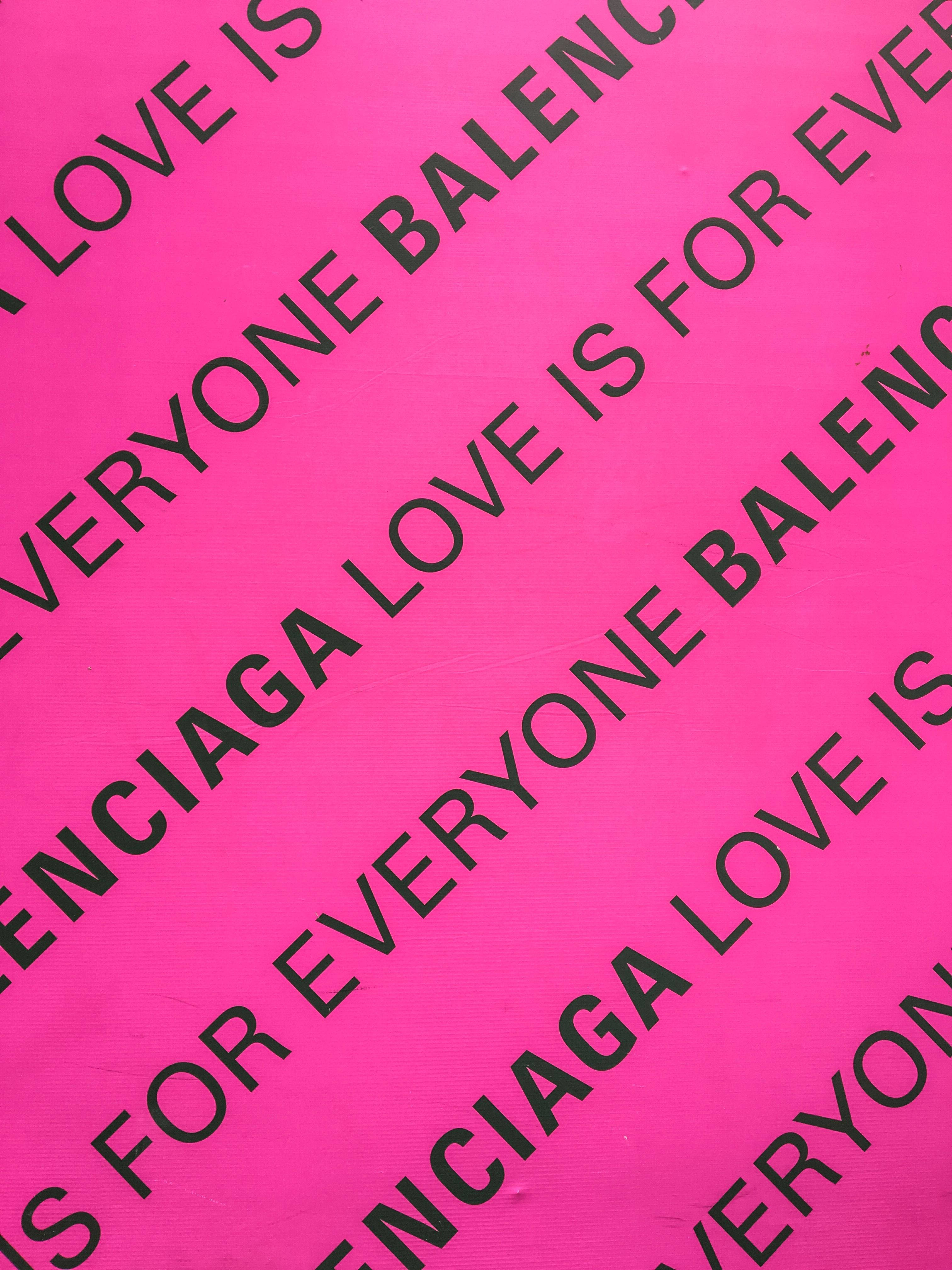 Balenciaga 桌布 壁紙 — 充滿活力的粉紅色壁紙，帶有重複的黑色文字，以對角線條紋顯示「LOVE IS FOR EVERYONE BALENCIAGA」。