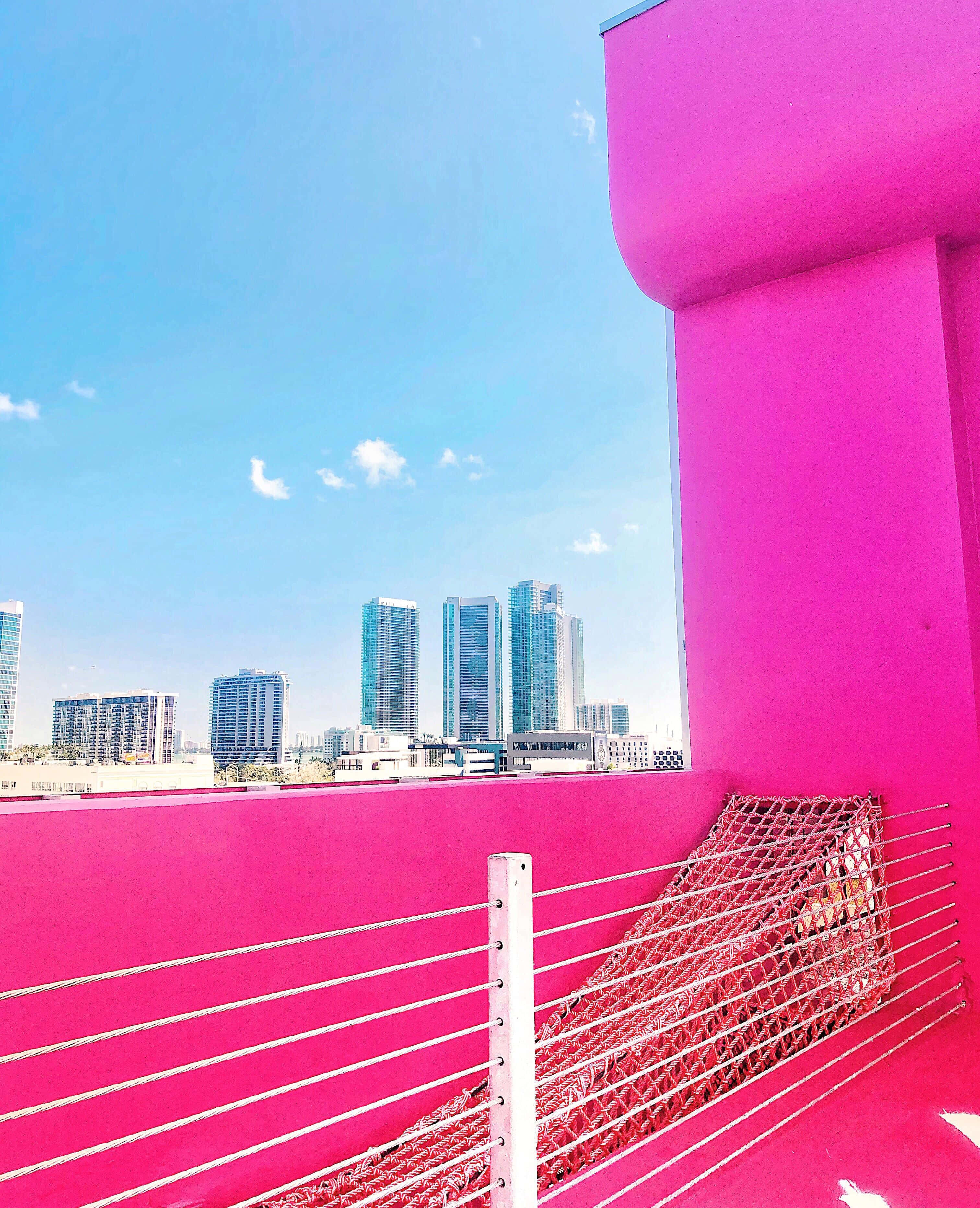 Miami 桌布 壁紙 — 充滿活力的粉紅色屋頂陽台，俯瞰著晴朗藍天白雲下的現代玻璃摩天大樓。