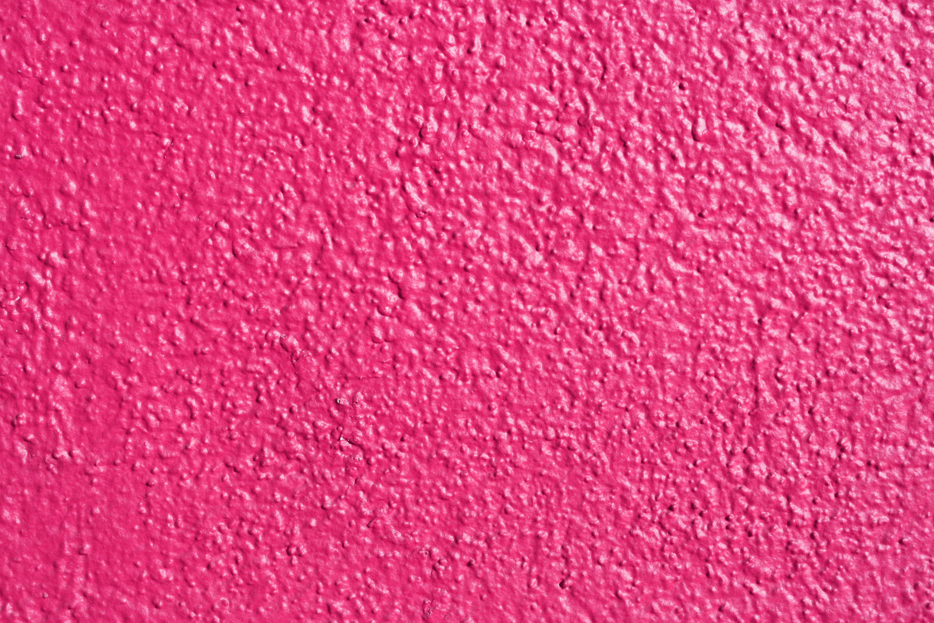 Pink Texture 桌布 壁紙 — 充滿活力的粉紅色灰泥牆，表面粗糙有紋理，在均勻光線下呈現微妙的色彩變化。