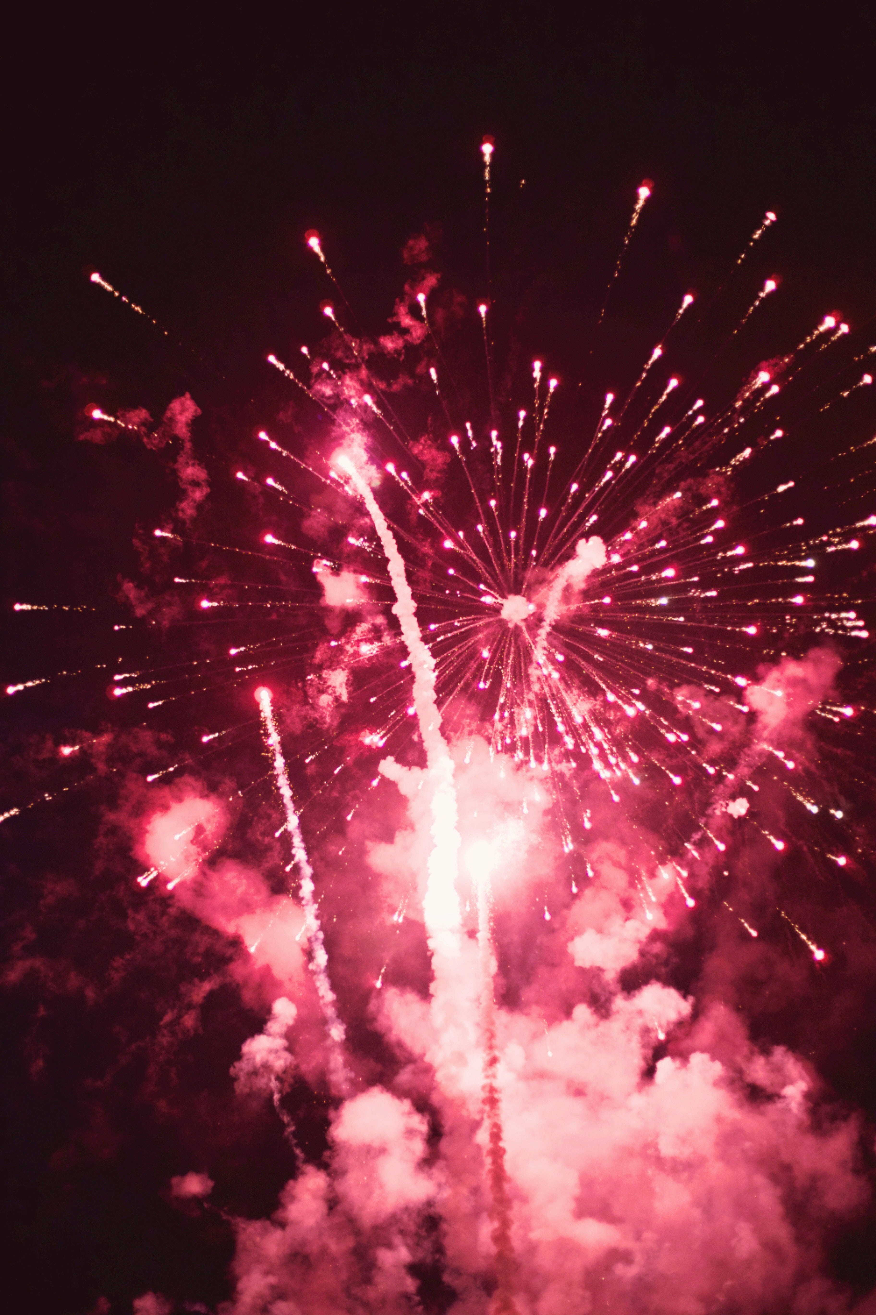Fireworks 桌布 壁紙 — 充滿活力的粉紅色煙火在黑暗的夜空中綻放出耀眼的光芒，下方有旋轉的煙霧。