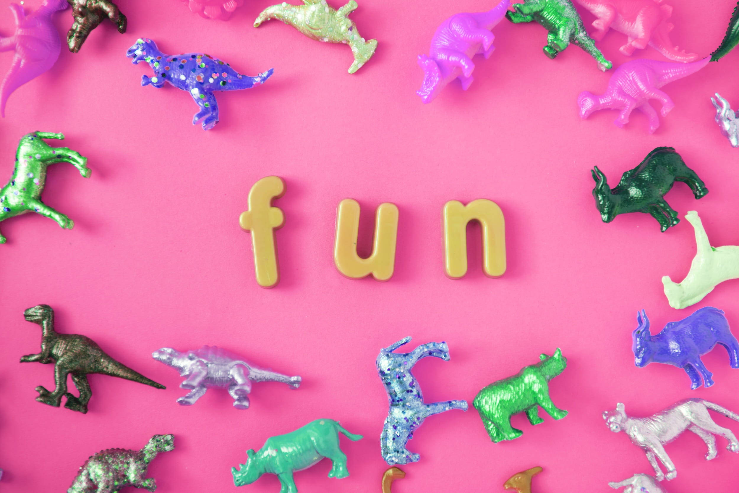 Cute Dinosaur 桌布 壁紙 — 充滿活力的粉紅色背景，閃亮的恐龍玩具圍繞著黃色字母的「fun」字。