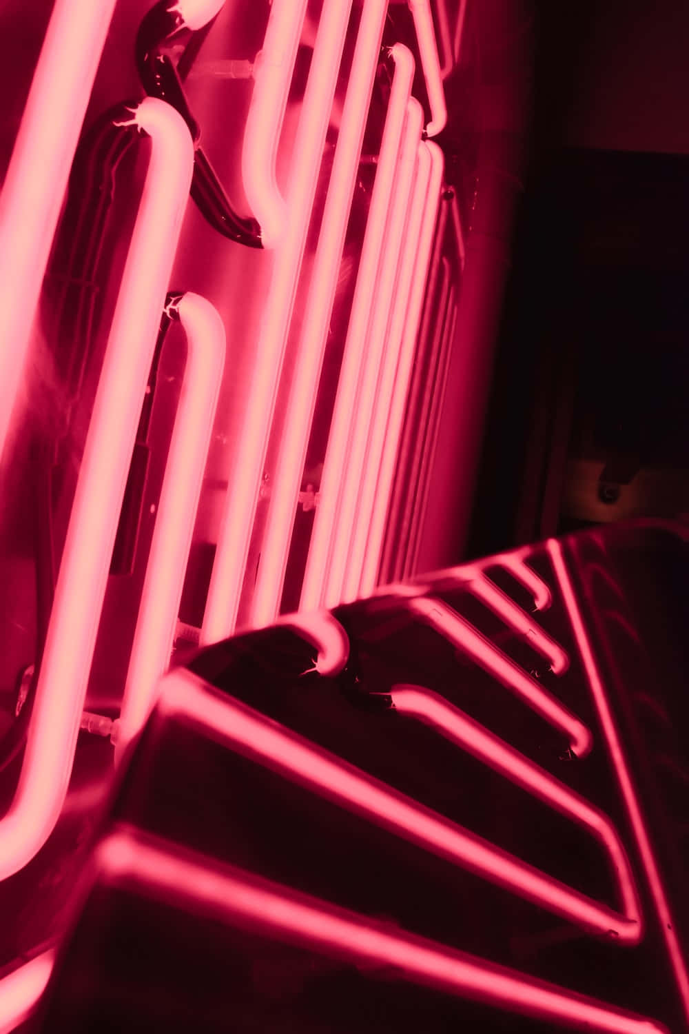 Neon Pink 桌布 壁紙 — 充滿活力的粉紅色霓虹燈管在黑暗的工業環境中發光，投射出銳利的幾何陰影。