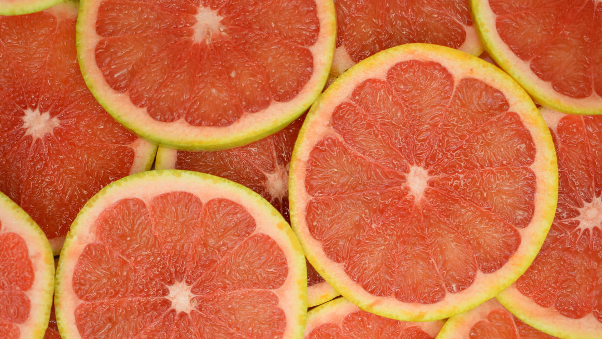 Pink Grapefruit 桌布 壁紙 — 充滿活力的粉紅葡萄柚切片特寫，展現分瓣的果肉和淺色果皮。