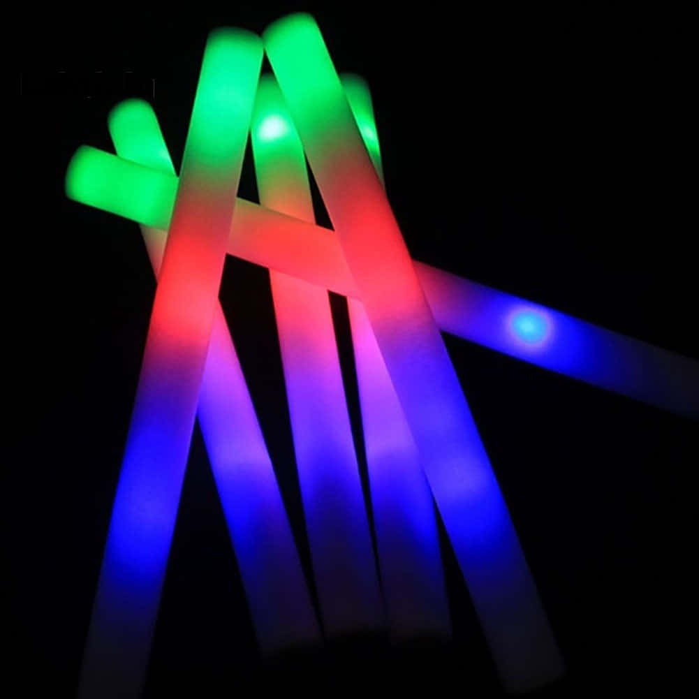 Light Up 桌布 壁紙 — 充滿活力的紅色、綠色和藍色發光棒在漆黑的背景下散發光芒，營造出節日的霓虹光輝。