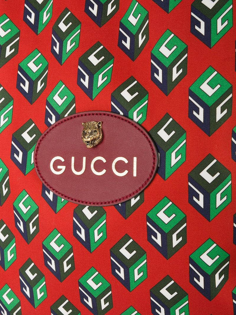 Gucci 桌布 壁紙 — 充滿活力的紅色布料，帶有重複的綠色和海軍藍GG立方體，以及中央帶有金色老虎頭的勃艮第Gucci標誌貼片。