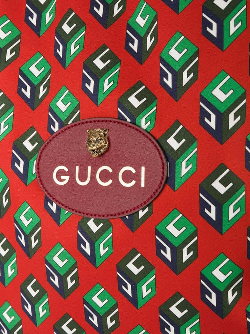 Gucci Pattern 桌布 壁紙 — 充滿活力的紅色背景，重複的綠色和深藍色Gucci方塊，中央有一個酒紅色皮革補丁，帶有金色老虎頭和白色標誌。
