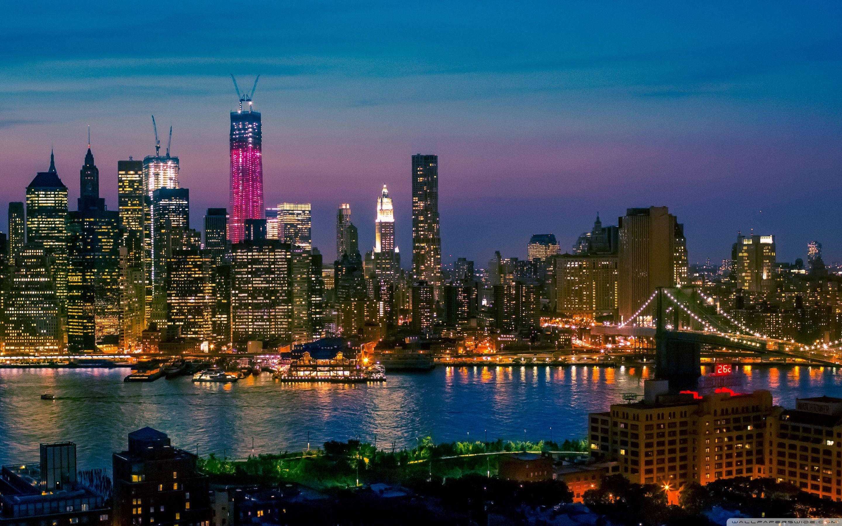 New York 桌布 壁紙 — 充滿活力的紐約暮色城市景觀，閃爍的摩天大樓和燈火通明的橋樑倒映在河中。