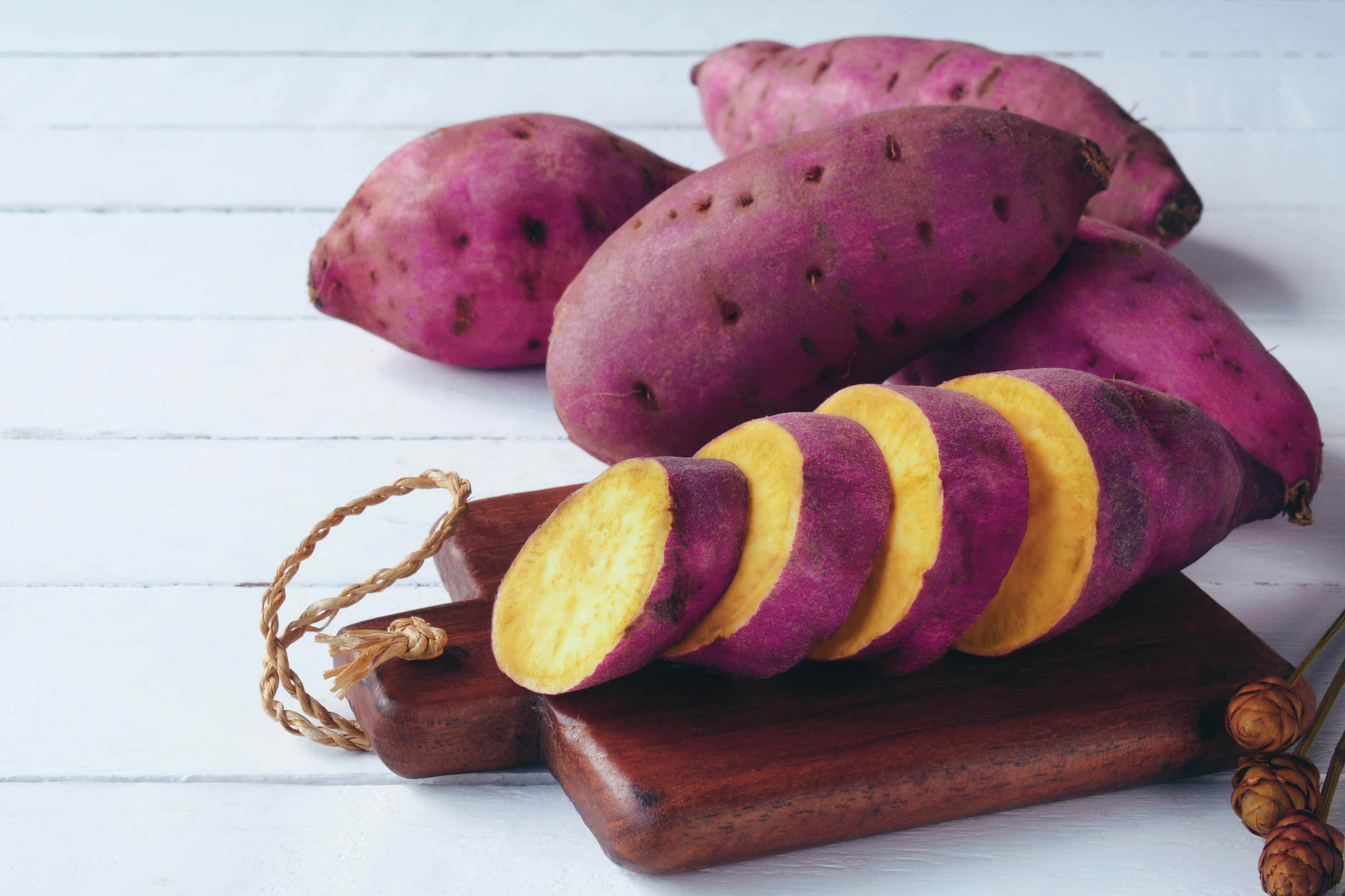 Purple Potato 桌布 壁紙 — 充滿活力的紫心番薯，內裡金黃，切片後擺放在質樸的木砧板上，背景是白色木質。
