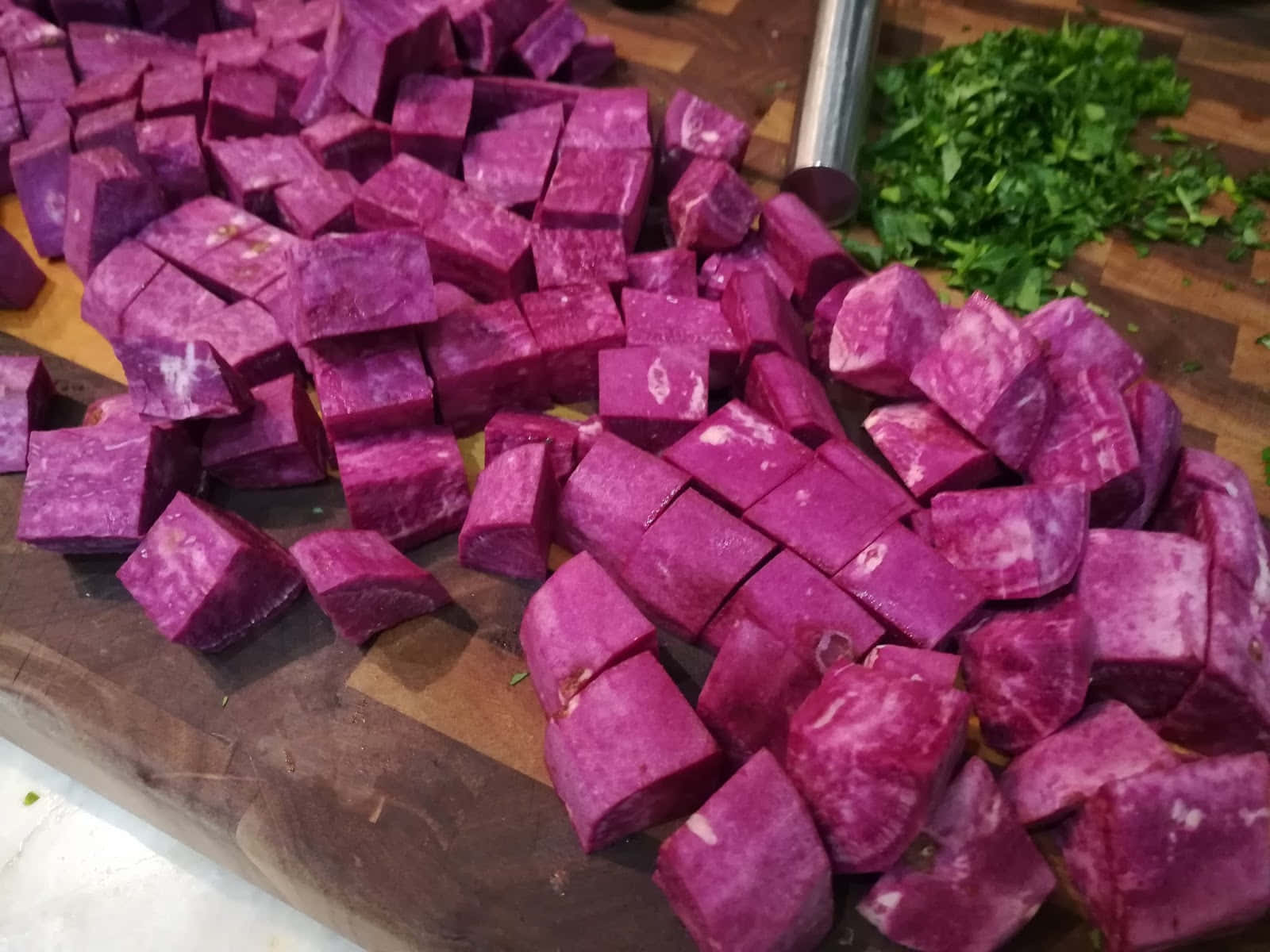 Purple Sweet Potato 桌布 壁紙 — 充滿活力的紫色地瓜塊和新鮮綠色香草散落在質樸的木砧板上。