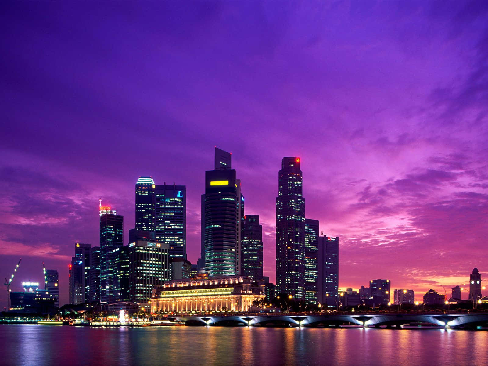 Singapore 桌布 壁紙 — 充滿活力的紫色日落照亮新加坡的天際線，摩天大樓倒映在下方平靜的水面上。