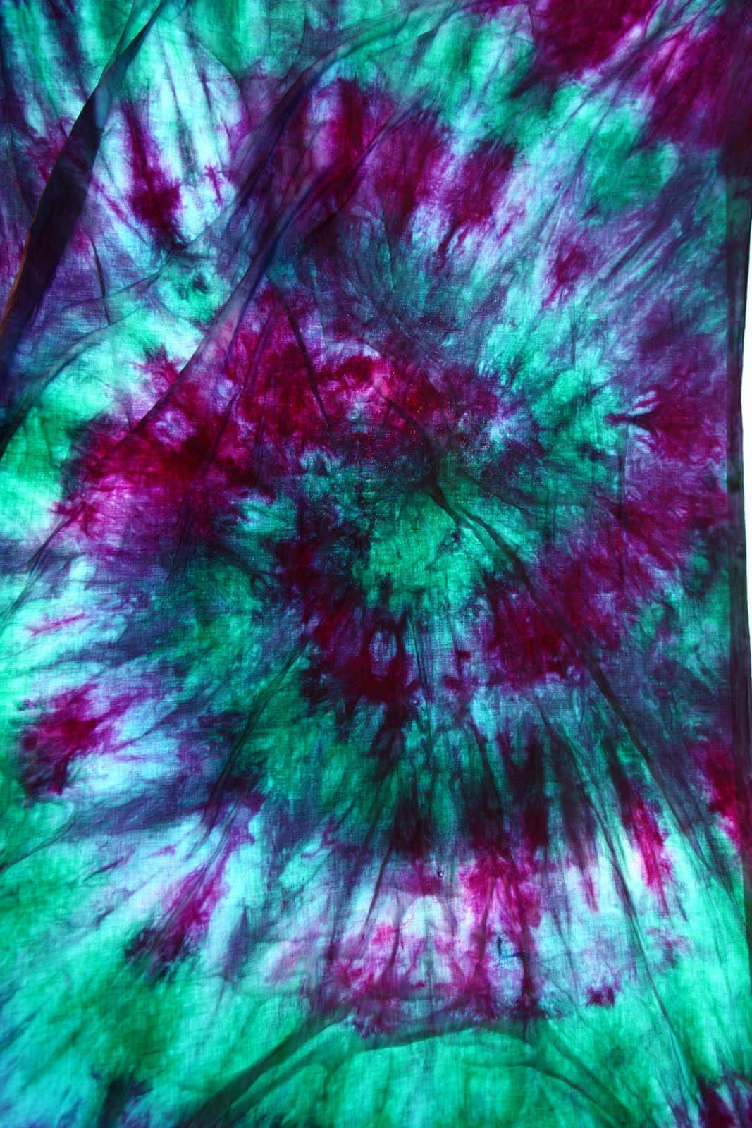 Purple Tie Dye 桌布 壁紙 — 充滿活力的紮染布料，呈現電光藍綠色和洋紅色的漩渦，帶有白色高光和布料褶皺。