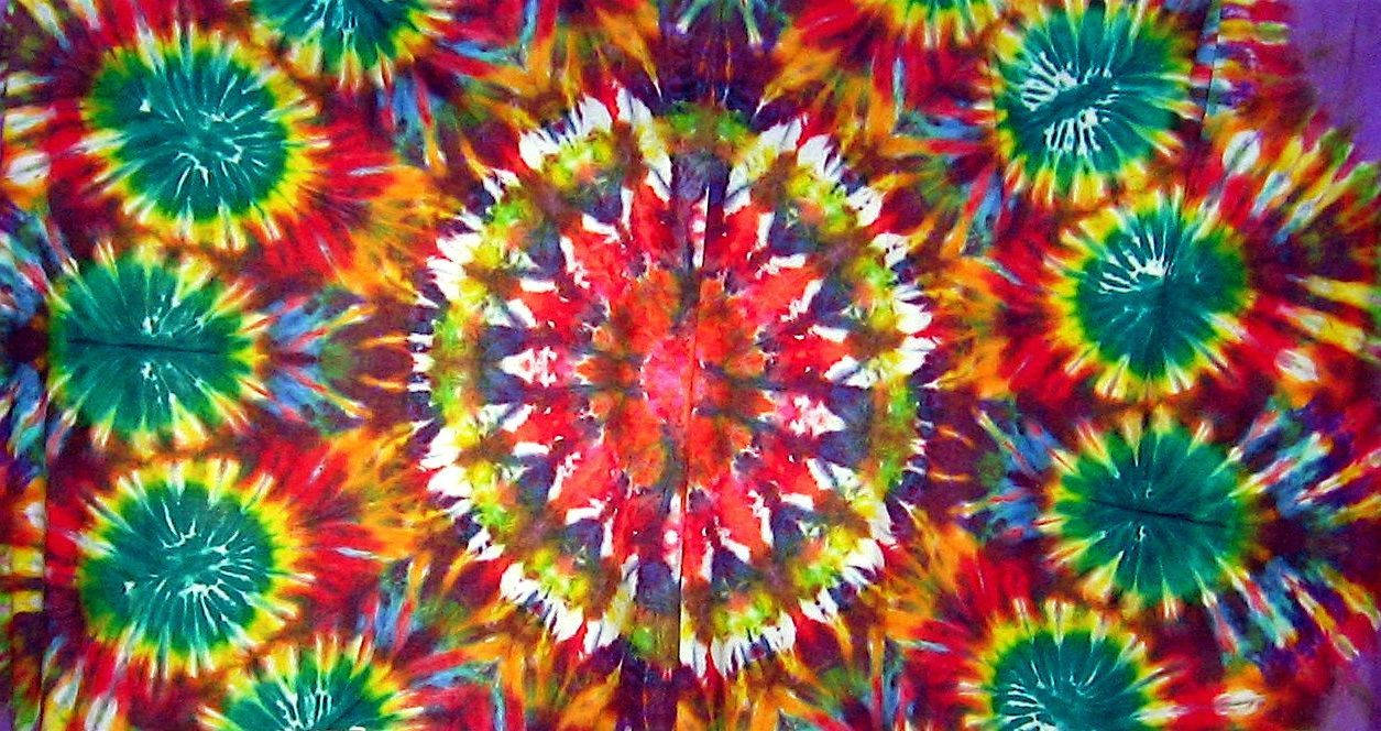 dye 桌布 壁紙 — 充滿活力的紮染布料，帶有紅色、綠色、黃色和白色的迷幻圓形圖案。
