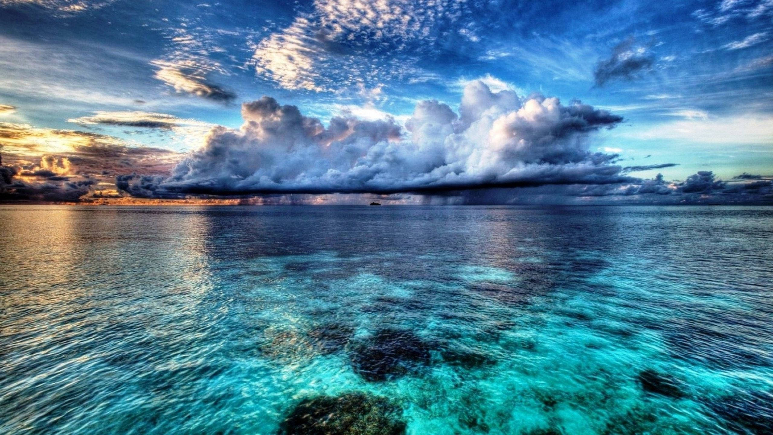 海洋 桌布 壁紙 — 充滿活力的綠松石海洋與戲劇性的天空相遇，地平線上有金色的日落雲和黑暗的風暴雲。