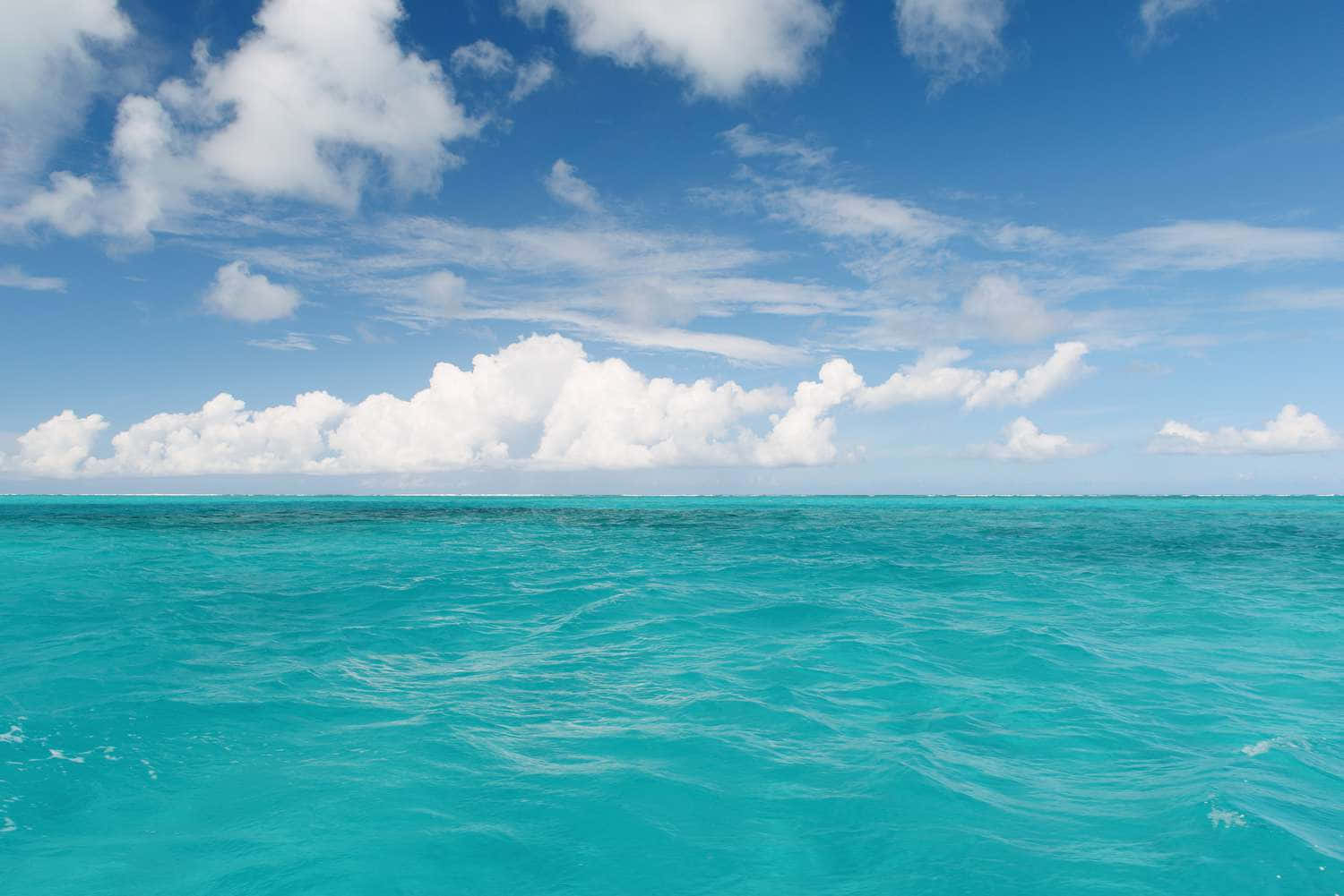 海洋藍 桌布 壁紙 — 充滿活力的綠松石色海浪在明亮的藍天下泛起漣漪，點綴著蓬鬆的白雲。