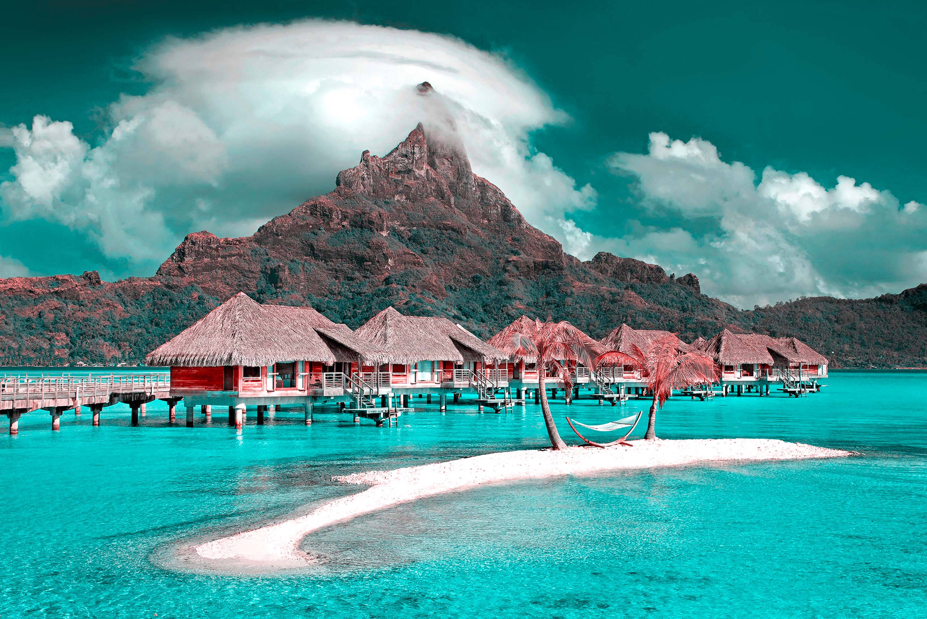 Maldives 桌布 壁紙 — 充滿活力的綠松石色潟湖，水上小屋和霧氣繚繞的火山峰在戲劇性的雲層下。