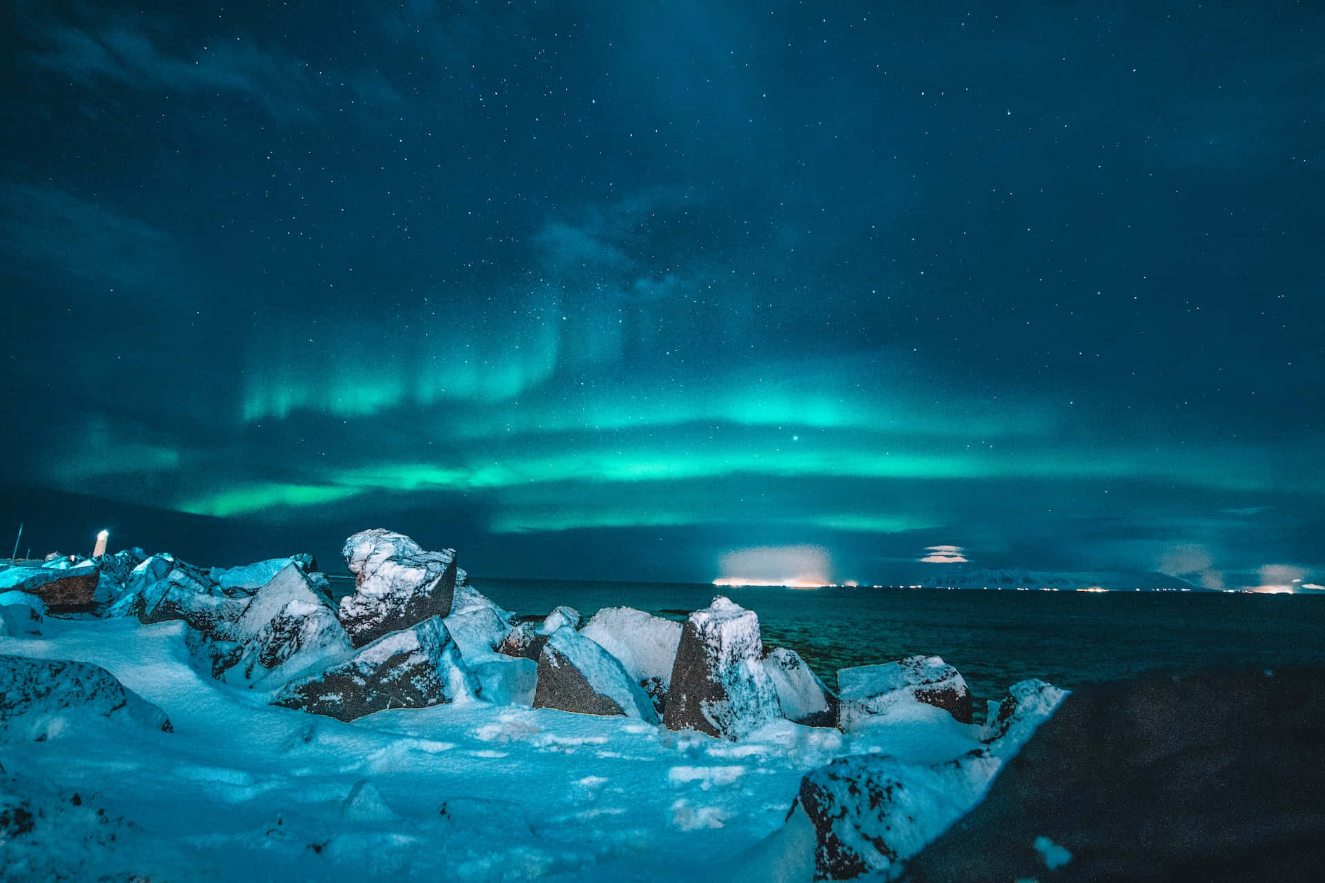 Iceland Desktop 桌布 壁紙 — 充滿活力的綠色北極光在冰封海洋旁的雪覆岩石上空，在繁星點點的夜空中舞動。