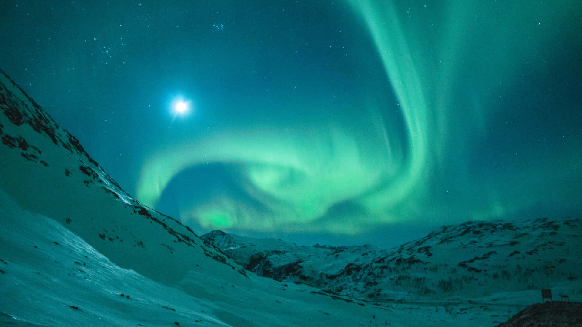 aurora borealis 桌布 壁紙 — 充滿活力的綠色北極光在明亮的月亮下，在白雪覆蓋的山峰上空，在繁星點點的夜空中舞動。