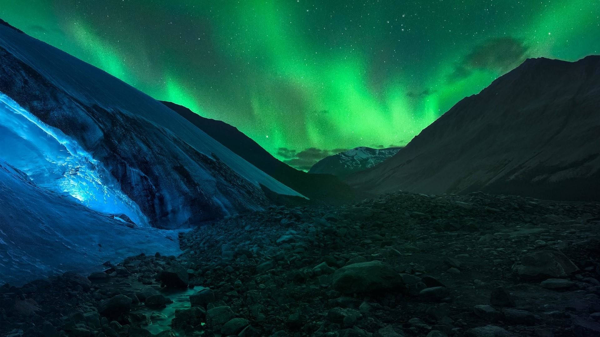 綠色天空 桌布 壁紙 — 充滿活力的綠色北極光在星空下，在積雪的山峰和發光的藍色冰川上舞動。
