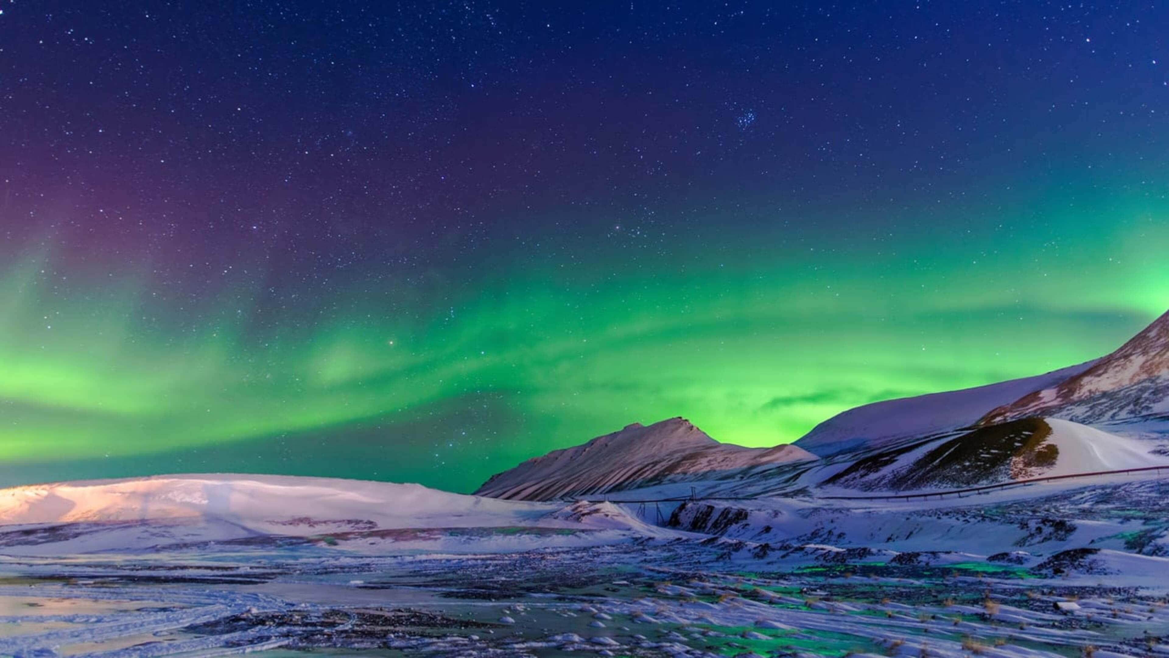 Aurora 桌布 壁紙 — 充滿活力的綠色北極光在星空下，於白雪覆蓋的山脈和冰凍苔原上空舞動。
