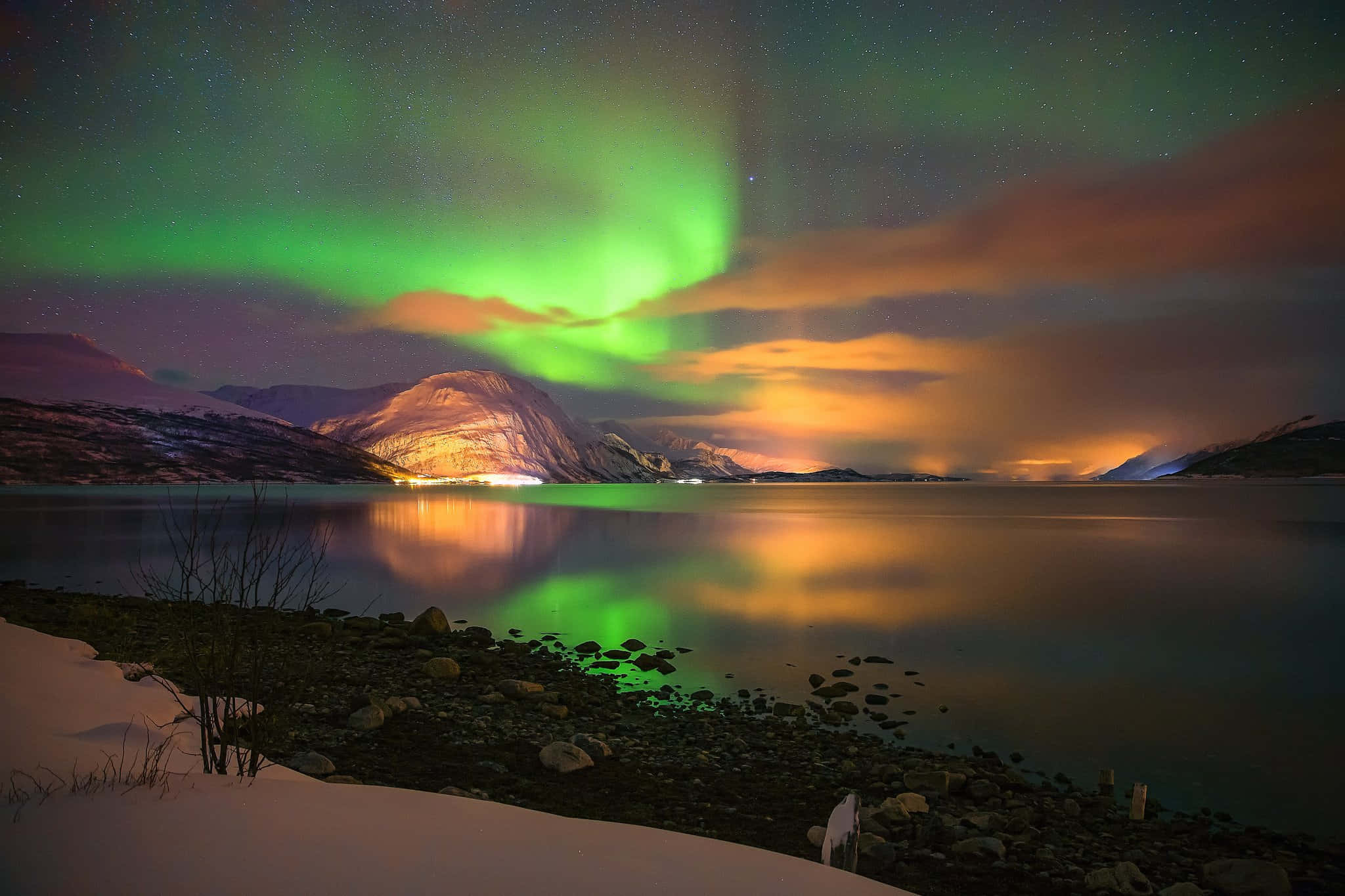aurora borealis 桌布 壁紙 — 充滿活力的綠色北極光在白雪覆蓋的山湖上舞動，倒映著星空和溫暖的雲彩。