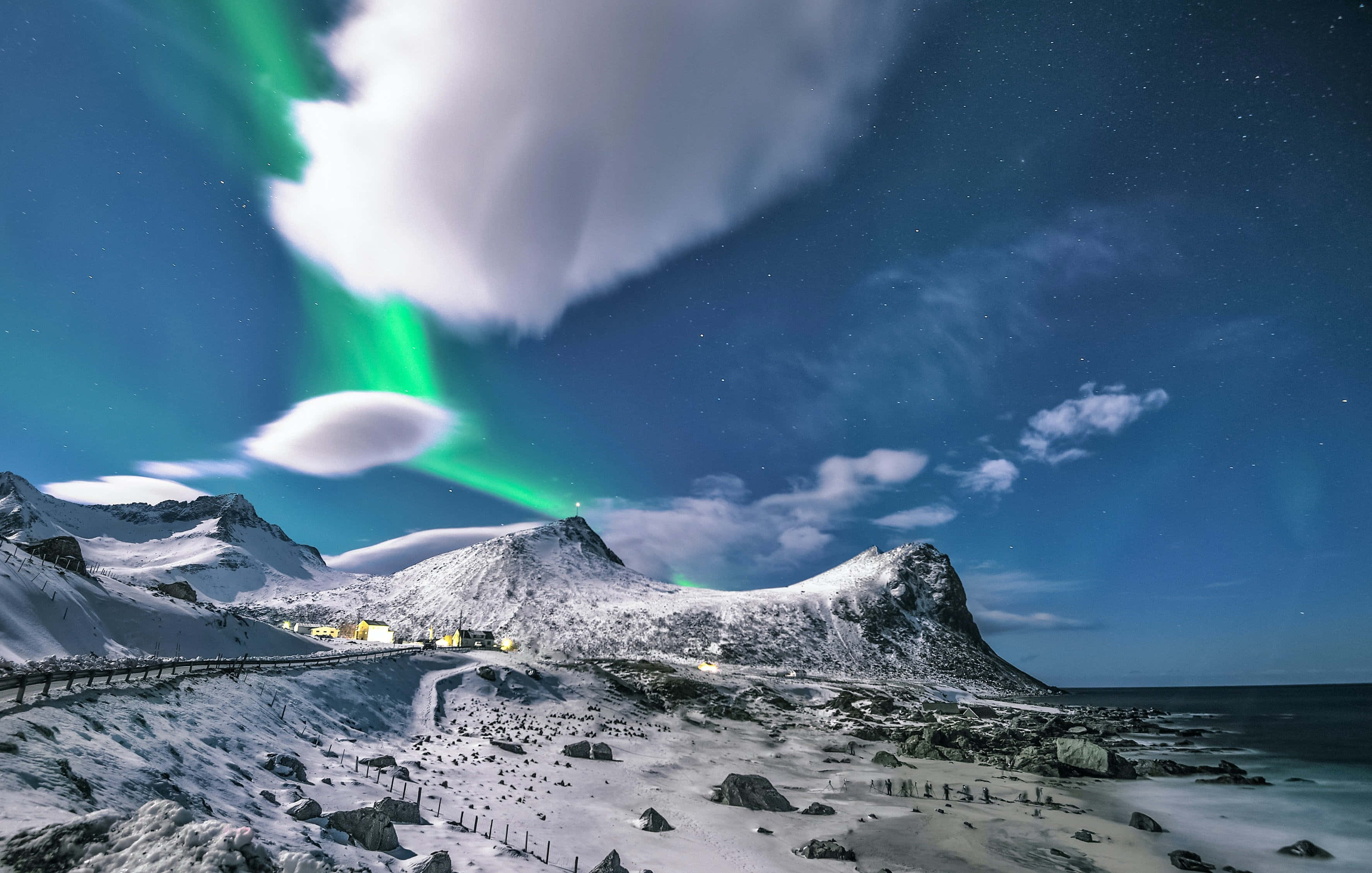 山景 桌布 壁紙 — 充滿活力的綠色北極光在白雪覆蓋的山脈和繁星點點的夜空上舞動，照耀著一個沿海村莊。