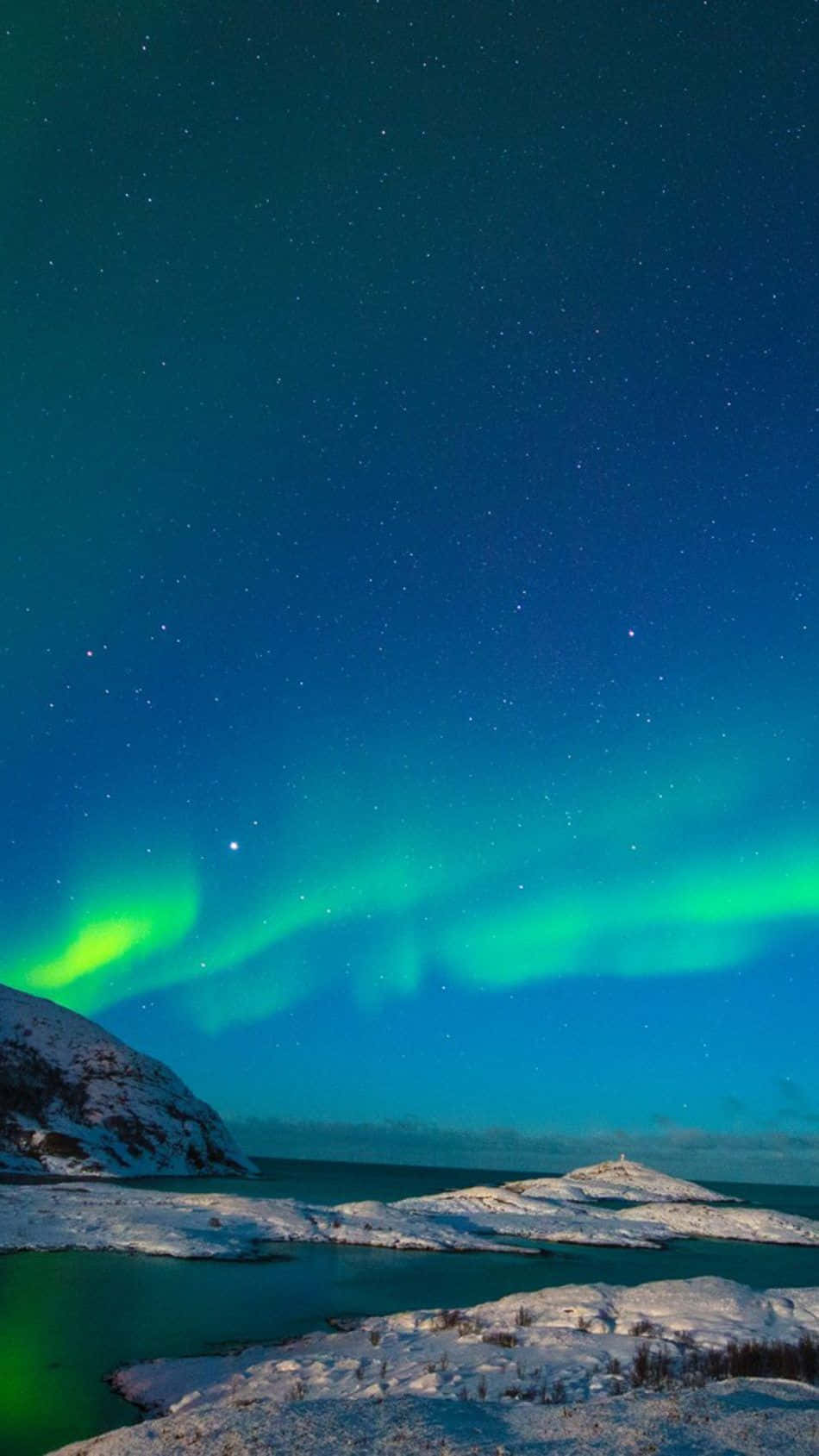 挪威 桌布 壁紙 — 充滿活力的綠色北極光在繁星點點的夜空中舞動，照耀著白雪覆蓋的北極凍原和冰冷的水域。
