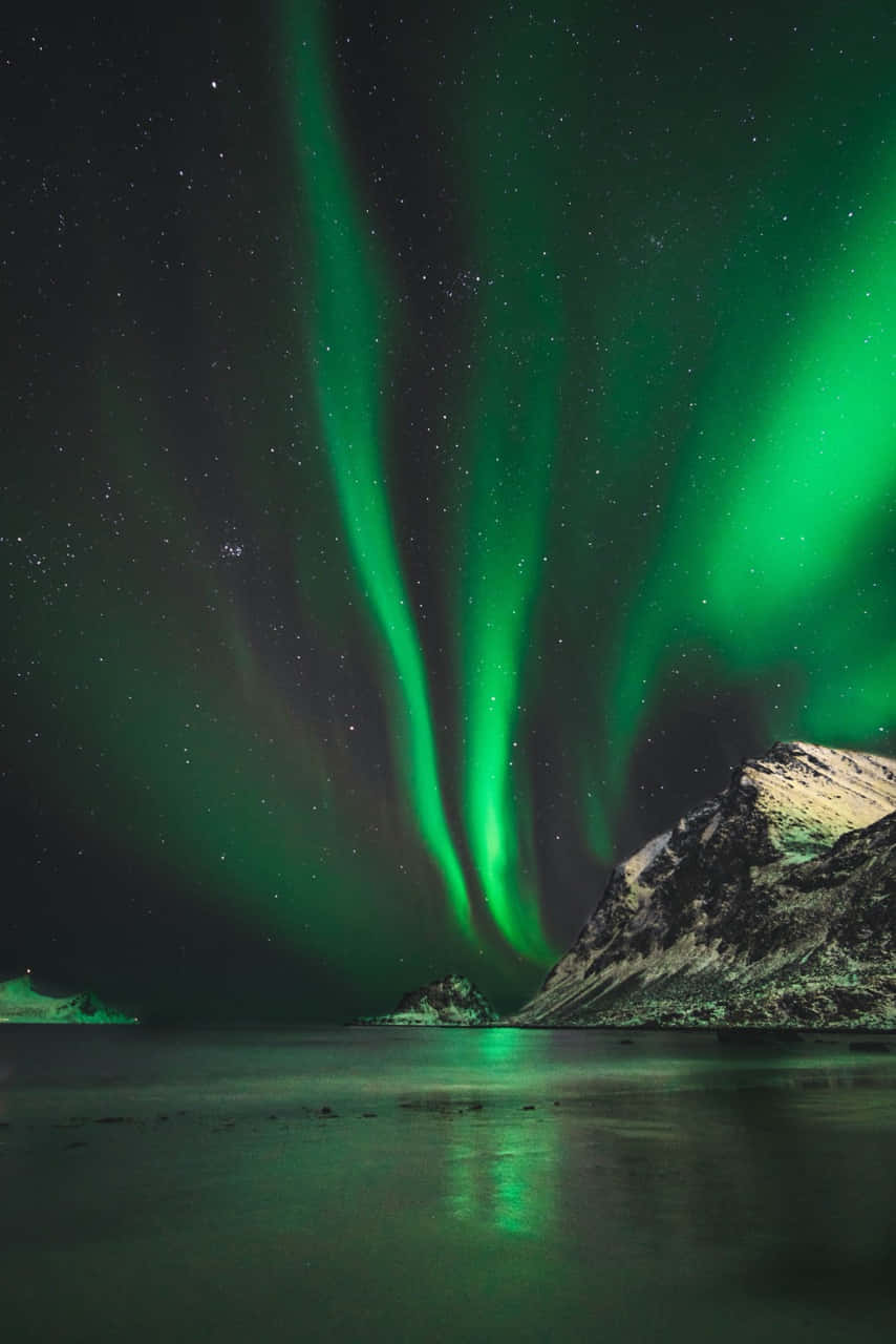 aurora borealis 桌布 壁紙 — 充滿活力的綠色北極光在繁星點點的夜空下，在積雪的山脈和寧靜的水面上舞動。