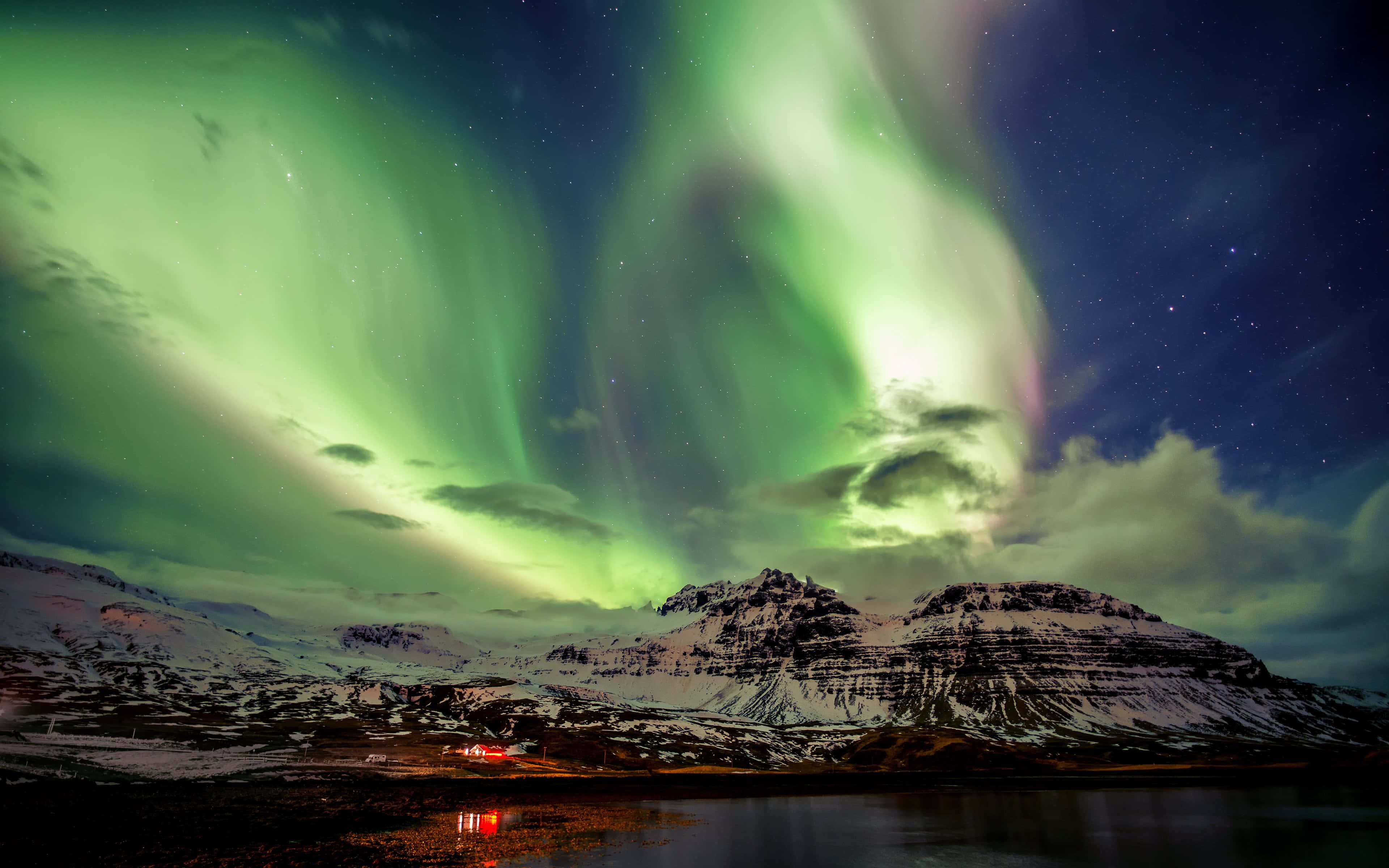 Iceland Desktop 桌布 壁紙 — 充滿活力的綠色北極光在繁星點點的夜空中舞動，下方是白雪覆蓋的山脈和寧靜如鏡的湖泊。