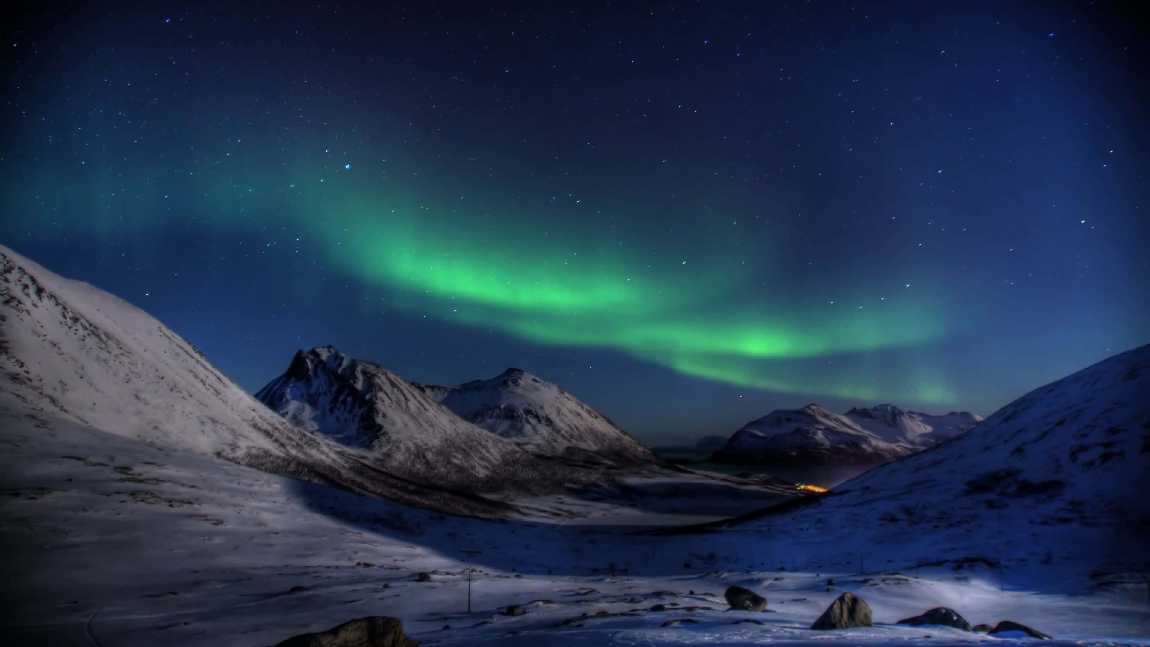 Aurora 桌布 壁紙 — 充滿活力的綠色北極光在繁星點點的夜空下，在積雪的山峰上舞動。