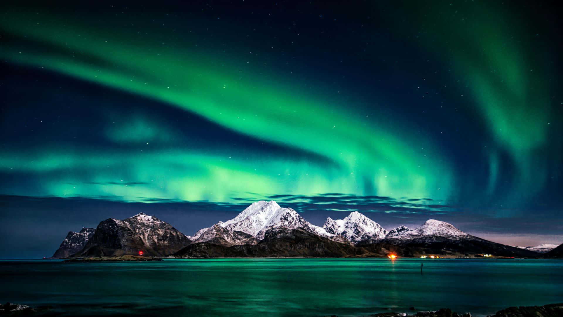 aurora borealis 桌布 壁紙 — 充滿活力的綠色北極光在繁星點點的夜空中舞動，映照在白雪覆蓋的山脈和寧靜的反射水面上。