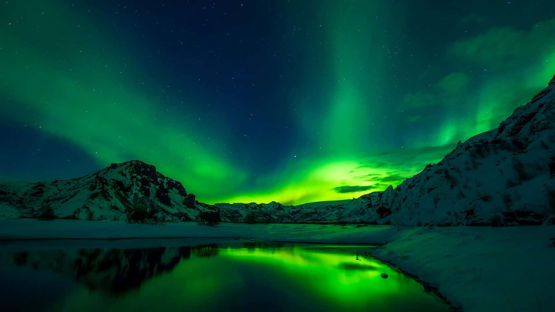 North Pole 桌布 壁紙 — 充滿活力的綠色北極光在繁星點點的夜空中舞動，映照著白雪覆蓋的山脈和反射的冰凍湖泊。