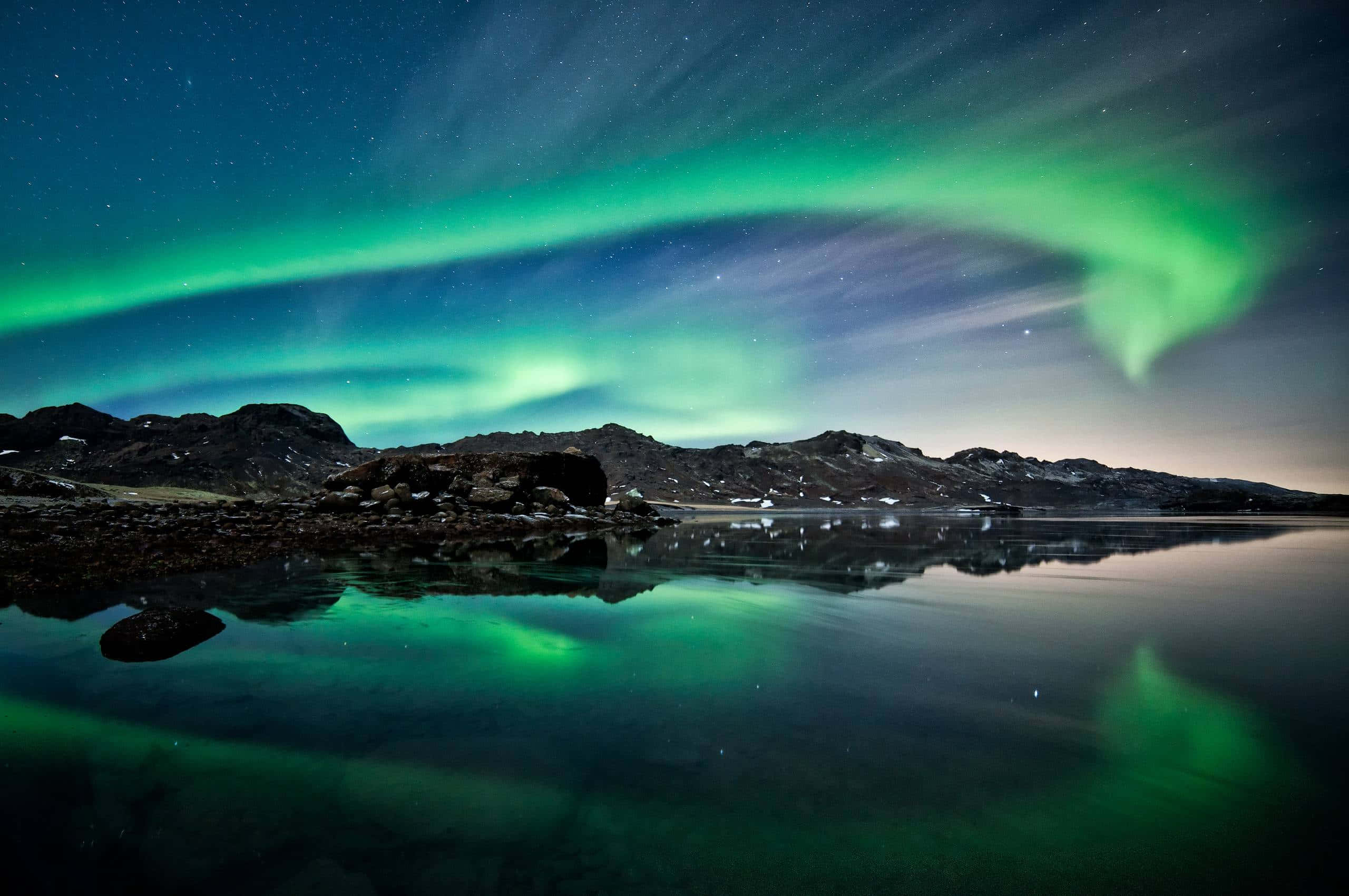 aurora borealis 桌布 壁紙 — 充滿活力的綠色北極光在繁星點點的夜空中舞動，倒映在崎嶇山脈下的平靜水域中。