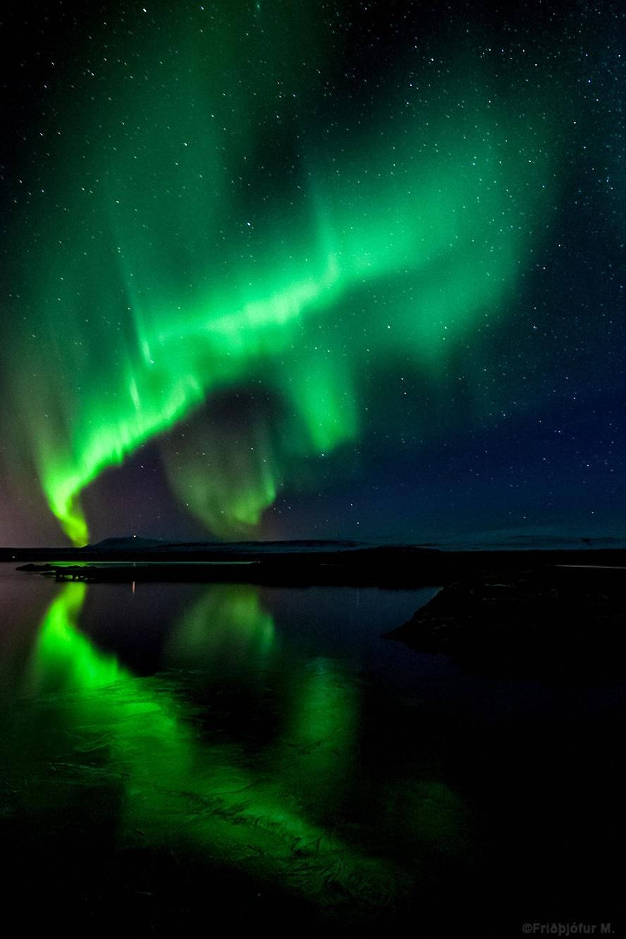 極光 桌布 壁紙 — 充滿活力的綠色北極光在繁星點點的夜空中舞動，完美地倒映在下方平靜的黑暗湖面上。