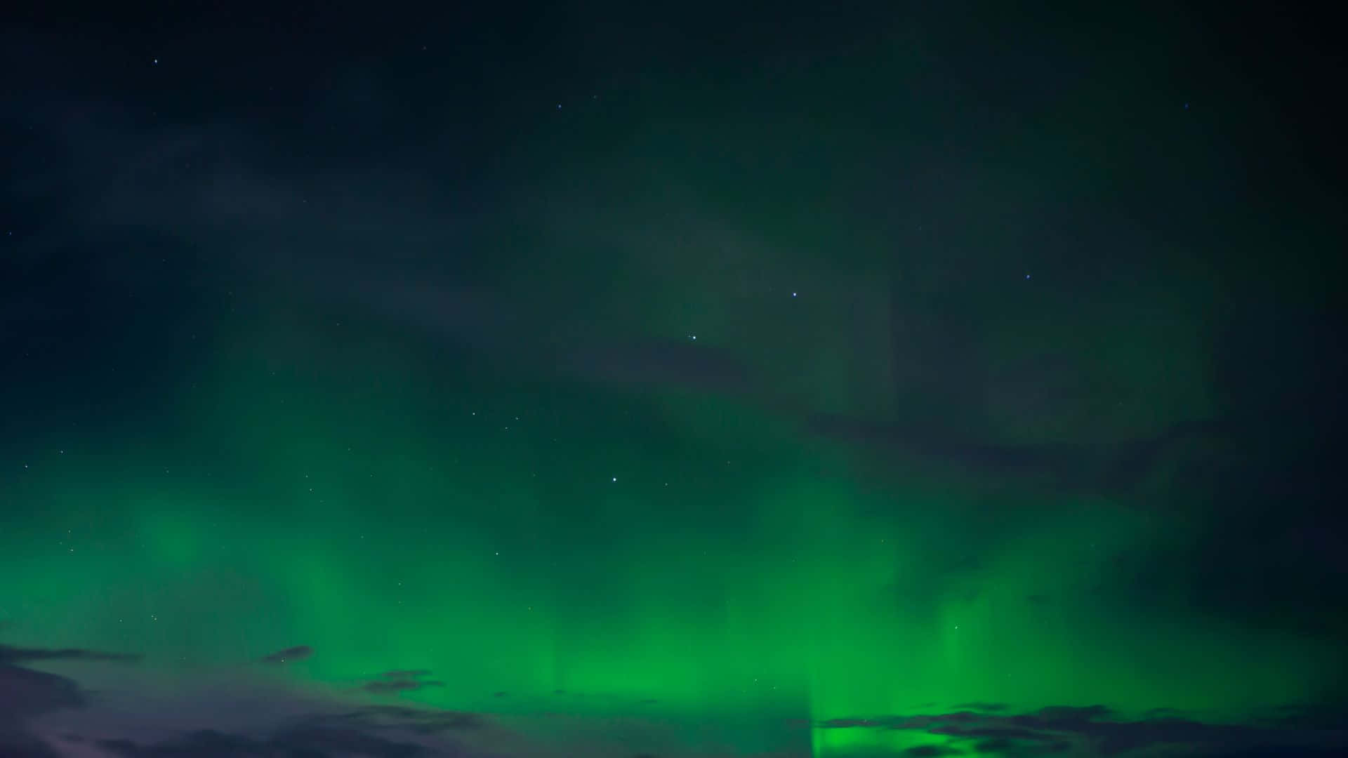 極光 桌布 壁紙 — 充滿活力的綠色北極光在繁星點點的夜空下舞動，下方有烏雲。