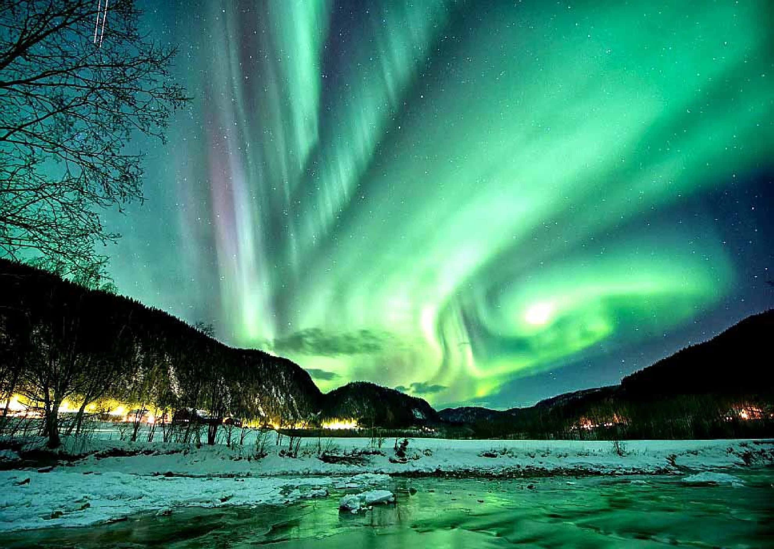Aurora 桌布 壁紙 — 充滿活力的綠色北極光在繁星點點的夜空中舞動，照耀著白雪覆蓋的山脈和冰封的河流。