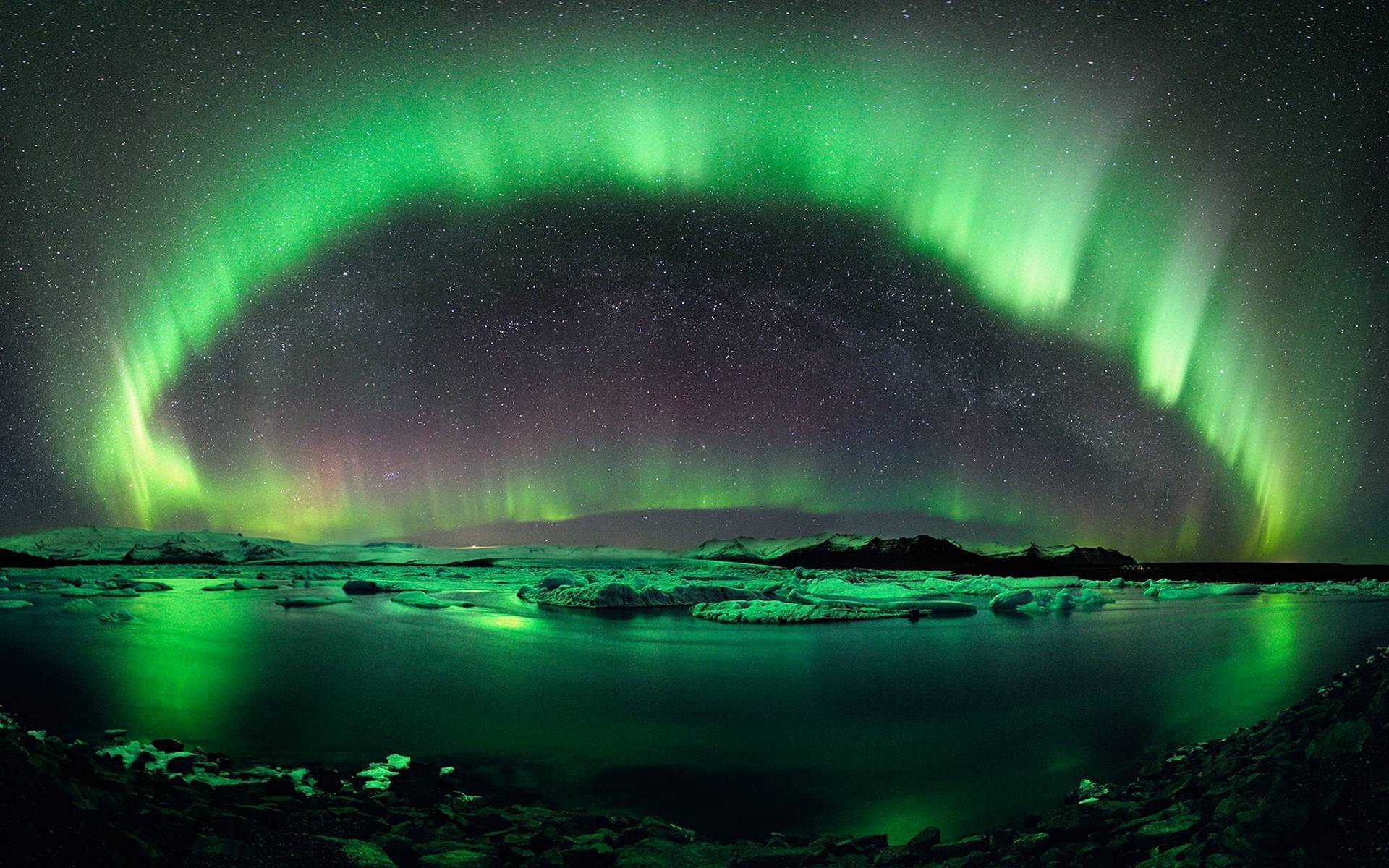 lights 桌布 壁紙 — 充滿活力的綠色北極光在繁星點點的夜空中拱起，反射在冰冷的水域和白雪覆蓋的土地上。