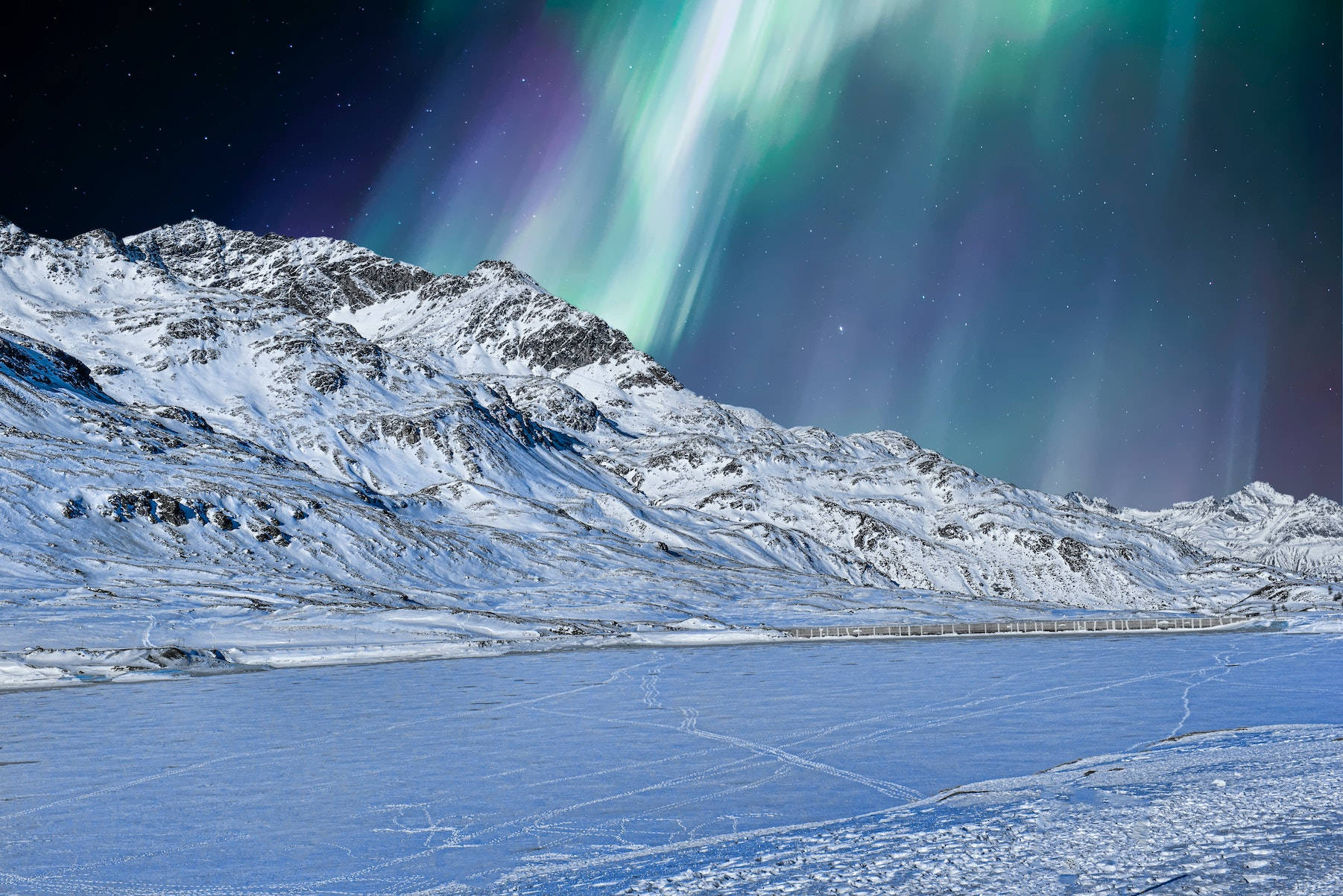 酷寒冬季 桌布 壁紙 — 充滿活力的綠色和紫色北極光在星空下舞動，照耀著白雪覆蓋的山脈和結冰的湖泊。