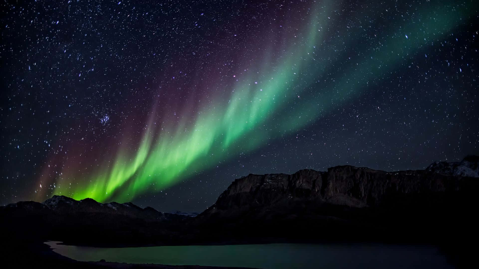 aurora borealis 桌布 壁紙 — 充滿活力的綠色和紫色北極光在繁星點點的夜空中舞動，映襯著黑暗的山巒輪廓和寧靜的湖泊。