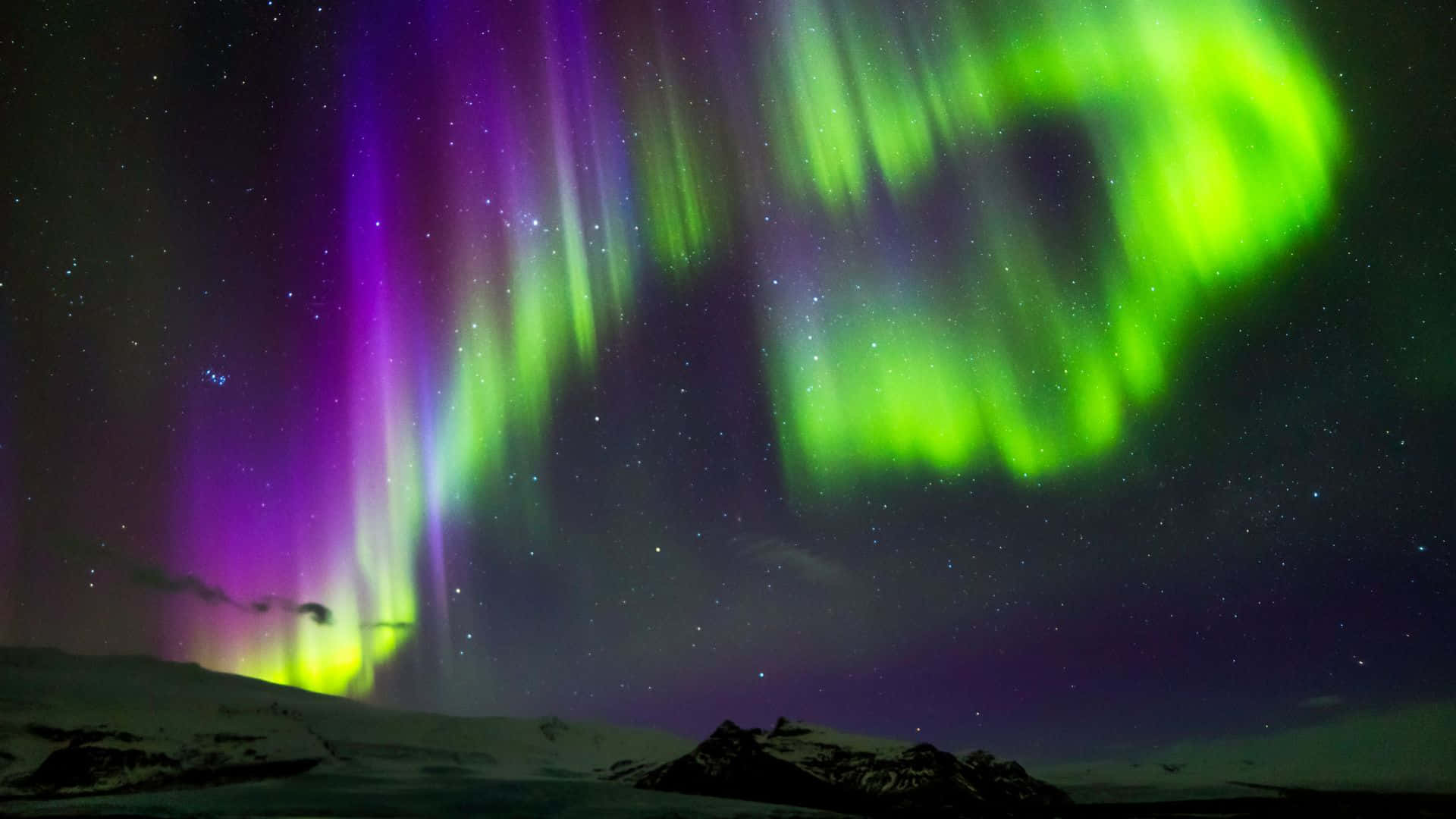 aurora borealis 桌布 壁紙 — 充滿活力的綠色和紫色極光在星空下的雪覆蓋山脈上空舞動。