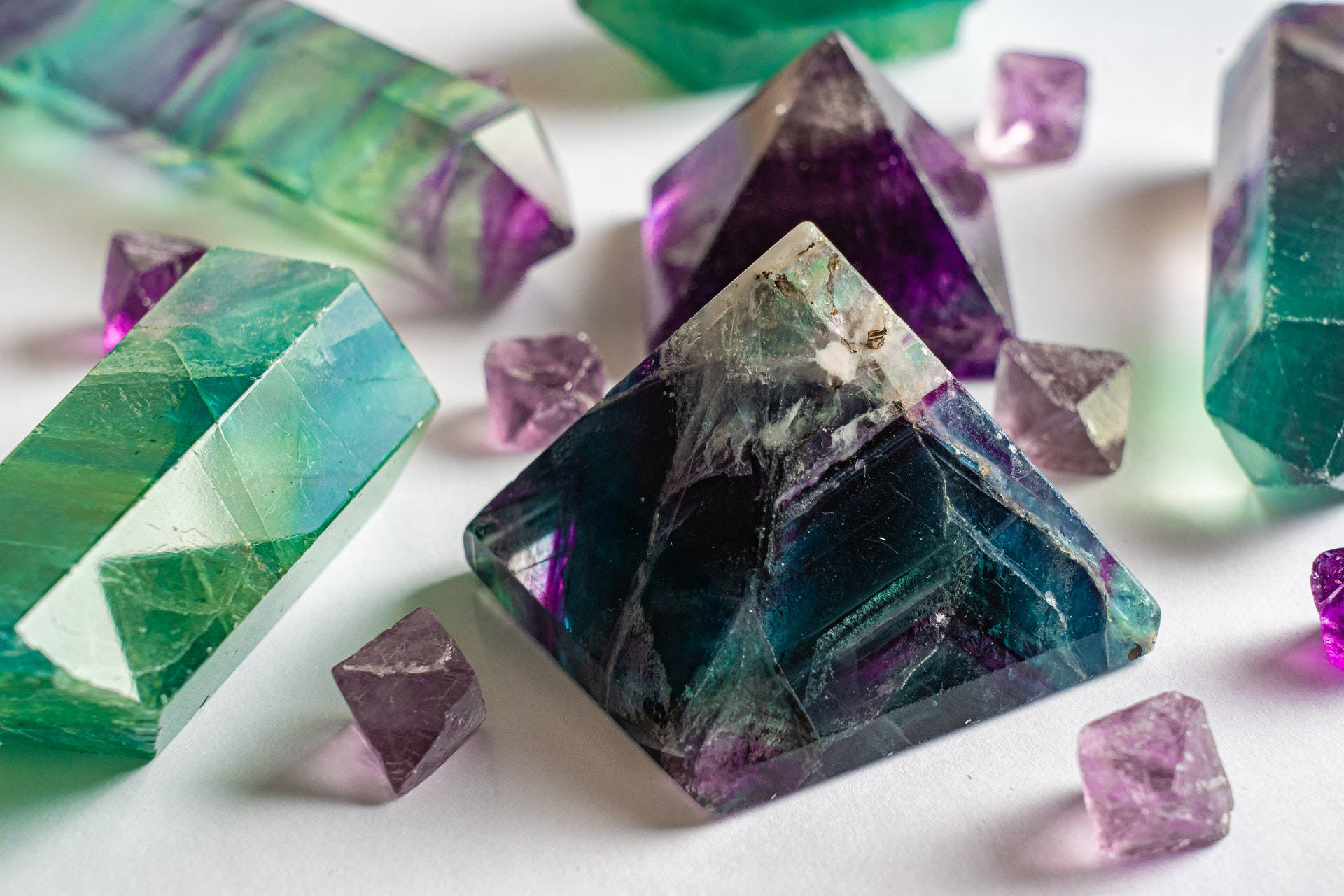 紫水晶 桌布 壁紙 — 充滿活力的綠色和紫色螢石晶體，帶有銳利的幾何切面，在白色表面上柔和光線下閃耀。