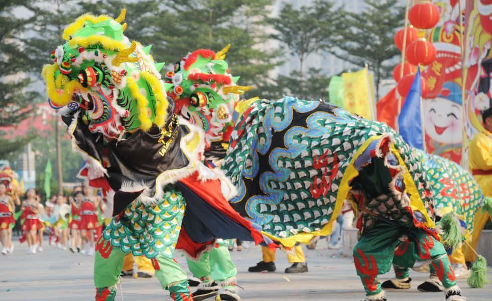 春節 桌布 壁紙 — 充滿活力的綠色和黃色舞龍者在節日街頭遊行中，伴隨著紅燈籠和歡呼的人群，精力充沛地表演。