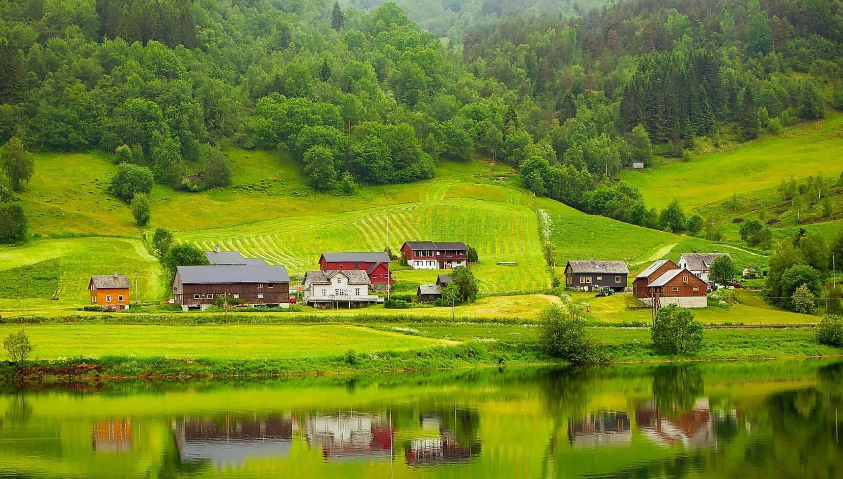 Beautiful Place 桌布 壁紙 — 充滿活力的綠色山丘上點綴著色彩繽紛的農舍，完美倒映在被茂密森林環繞的寧靜湖泊中。