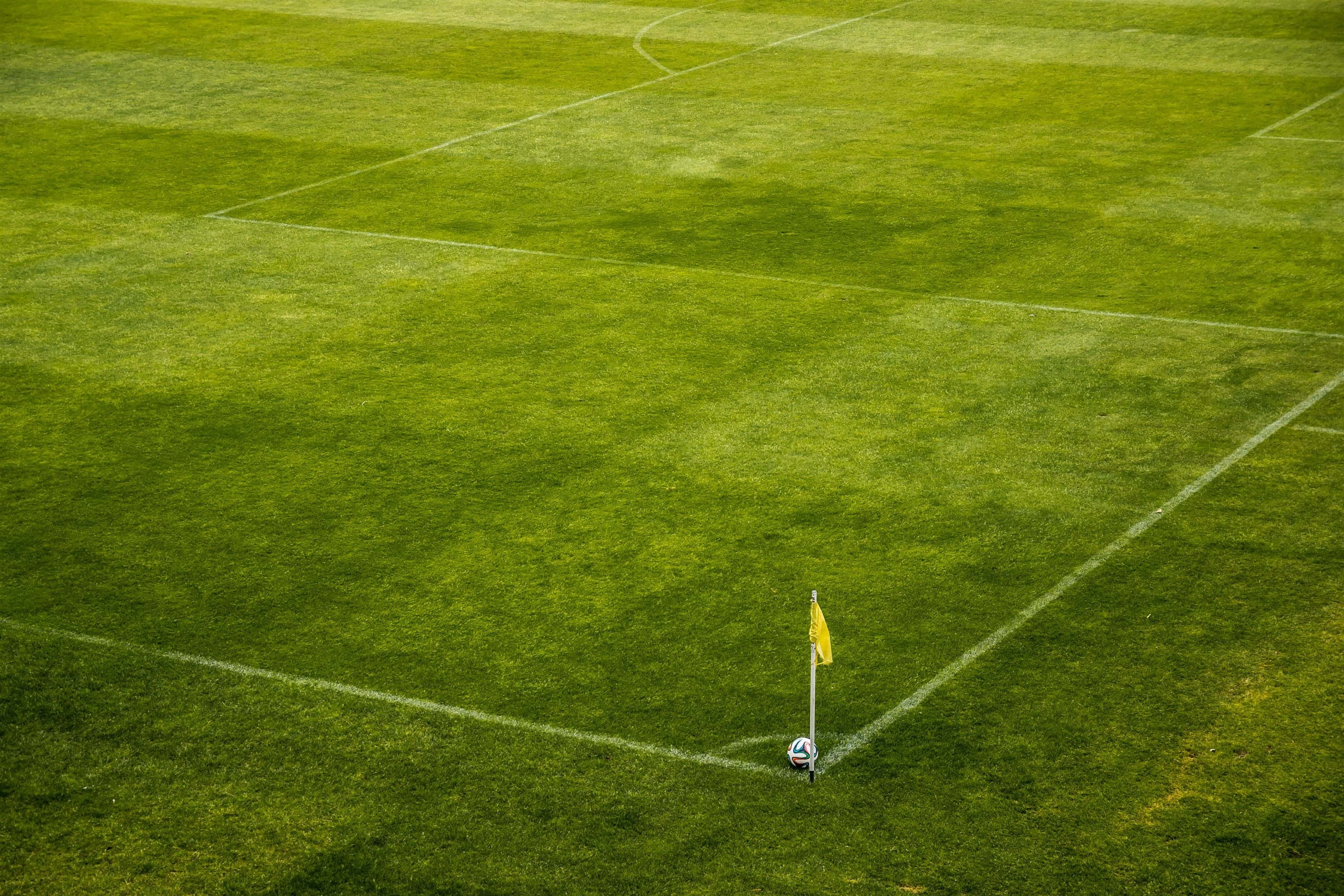 Football Field 桌布 壁紙 — 充滿活力的綠色足球場的鳥瞰圖，角落有黃色角旗和足球。