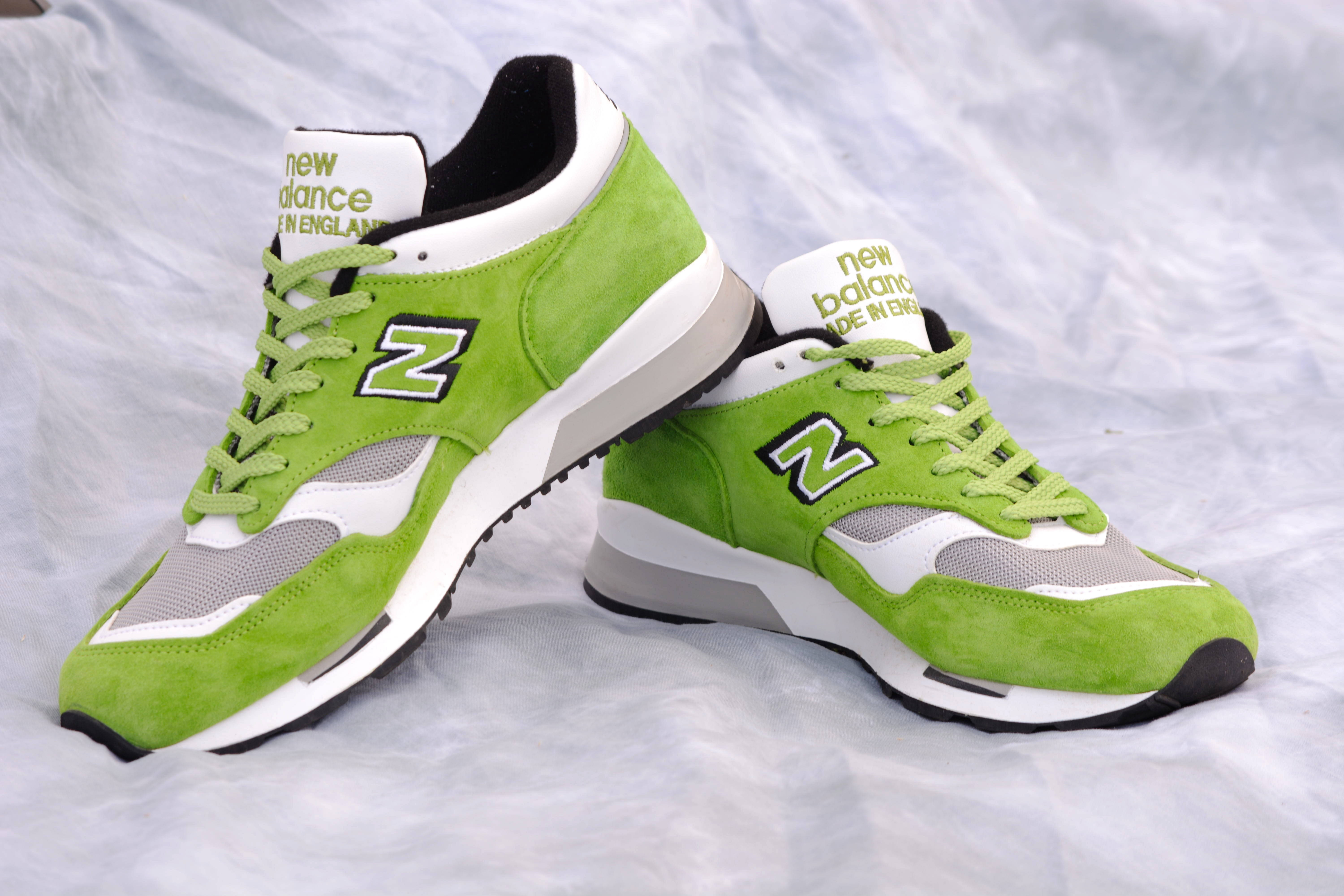 New 桌布 壁紙 — 充滿活力的萊姆綠色 New Balance 運動鞋，帶有白色點綴和黑色細節，放置在皺褶的銀色布料背景上。